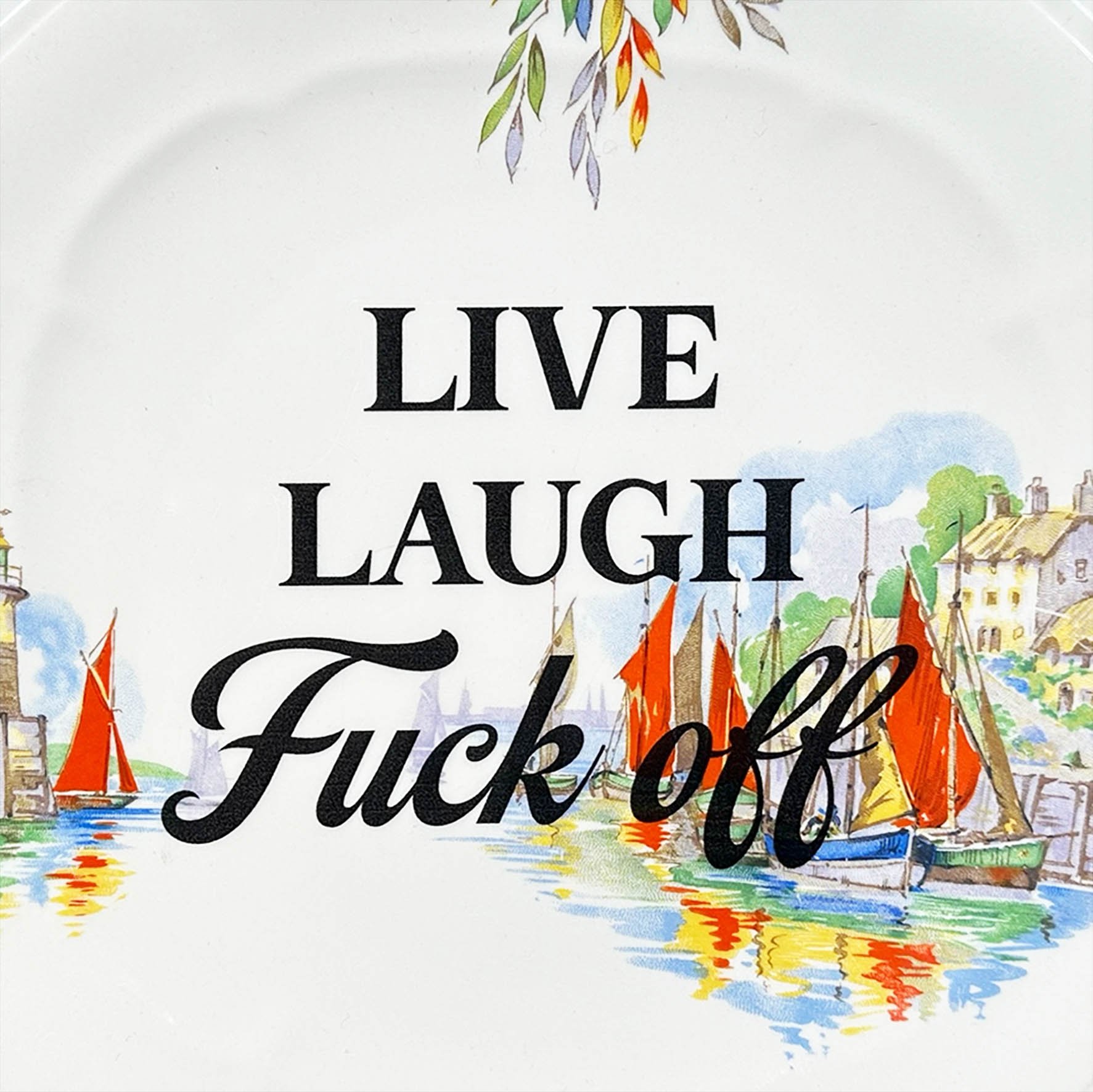 A vintage plate with the quote “live laugh fuck off” in black writing