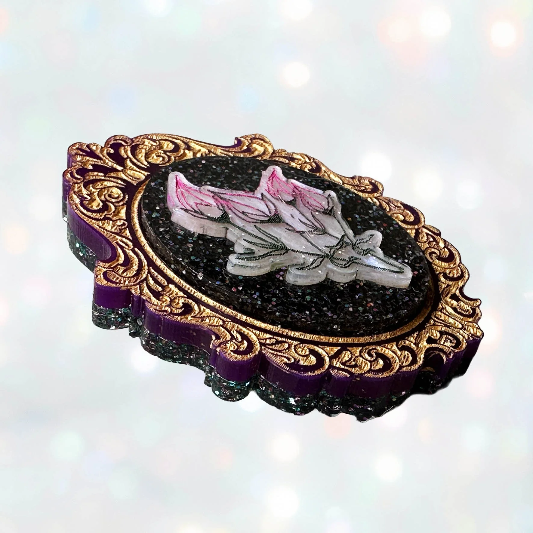 A laser cut acrylic cameo style brooch featuring a bunch of flowers within a purple and gold frame