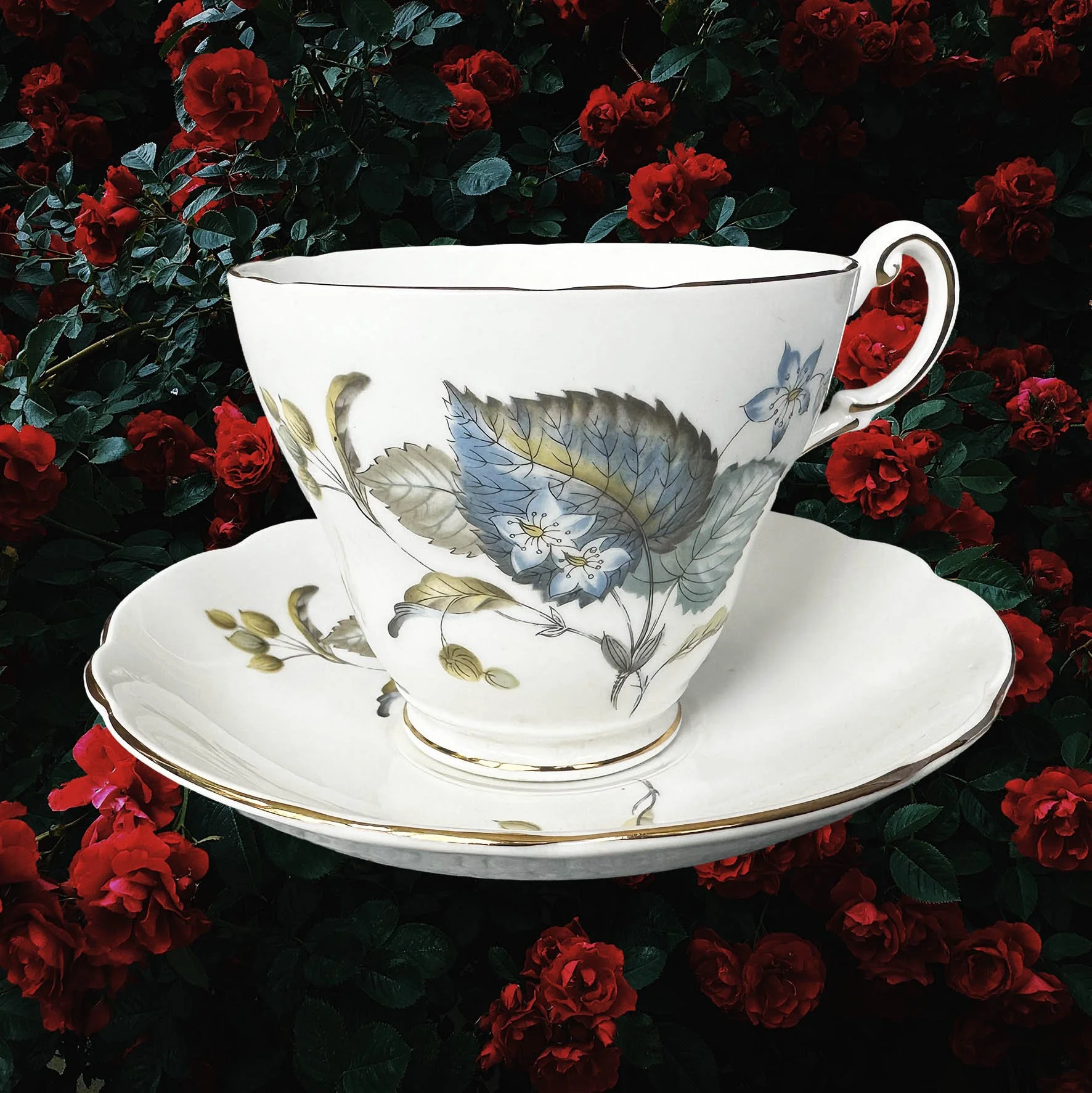 A vintage tea cup and saucer with a blue floral design and the words "let the good times be gin" in black cursive writing