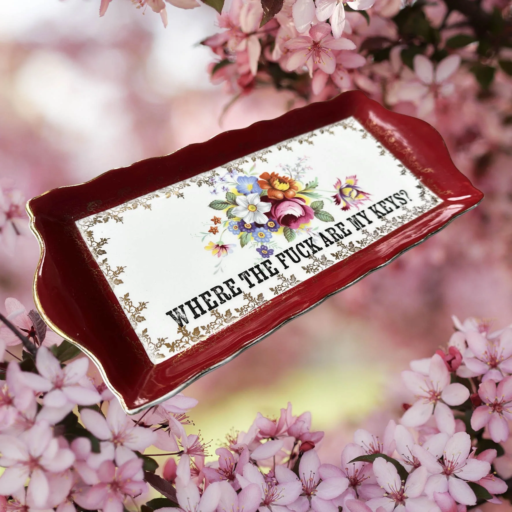 A vintage trinket dish with a red border and a floral design with the words “where the fuck are my keys?”