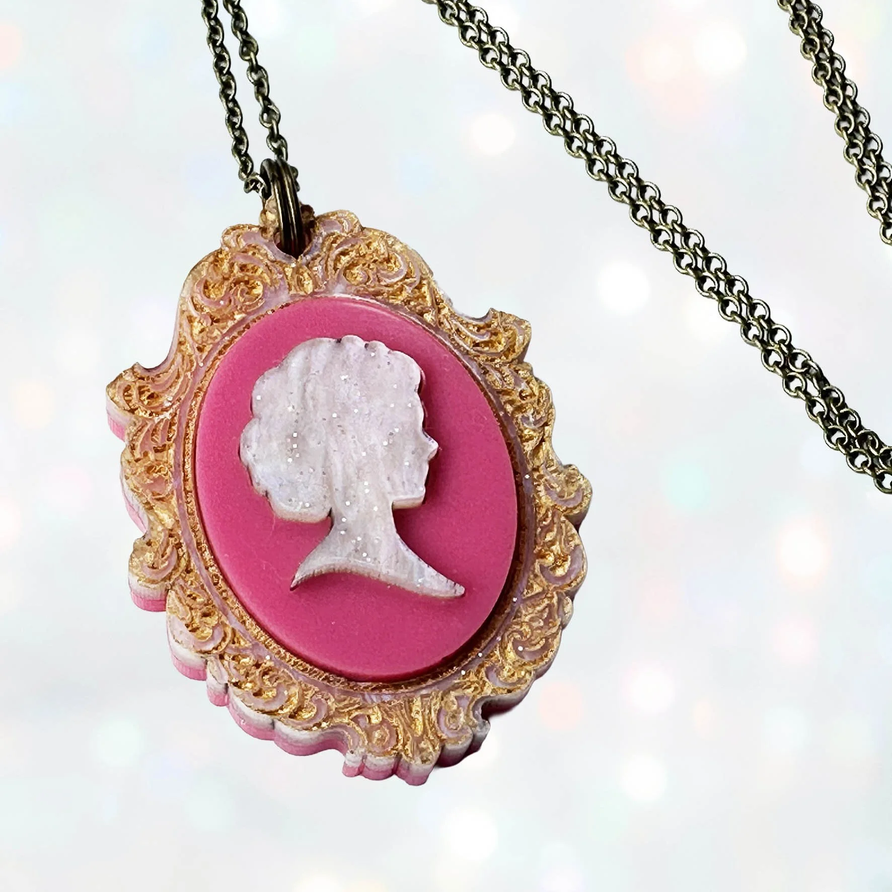 A laser cut pink and gold acrylic cameo style necklace featuring a silhouette