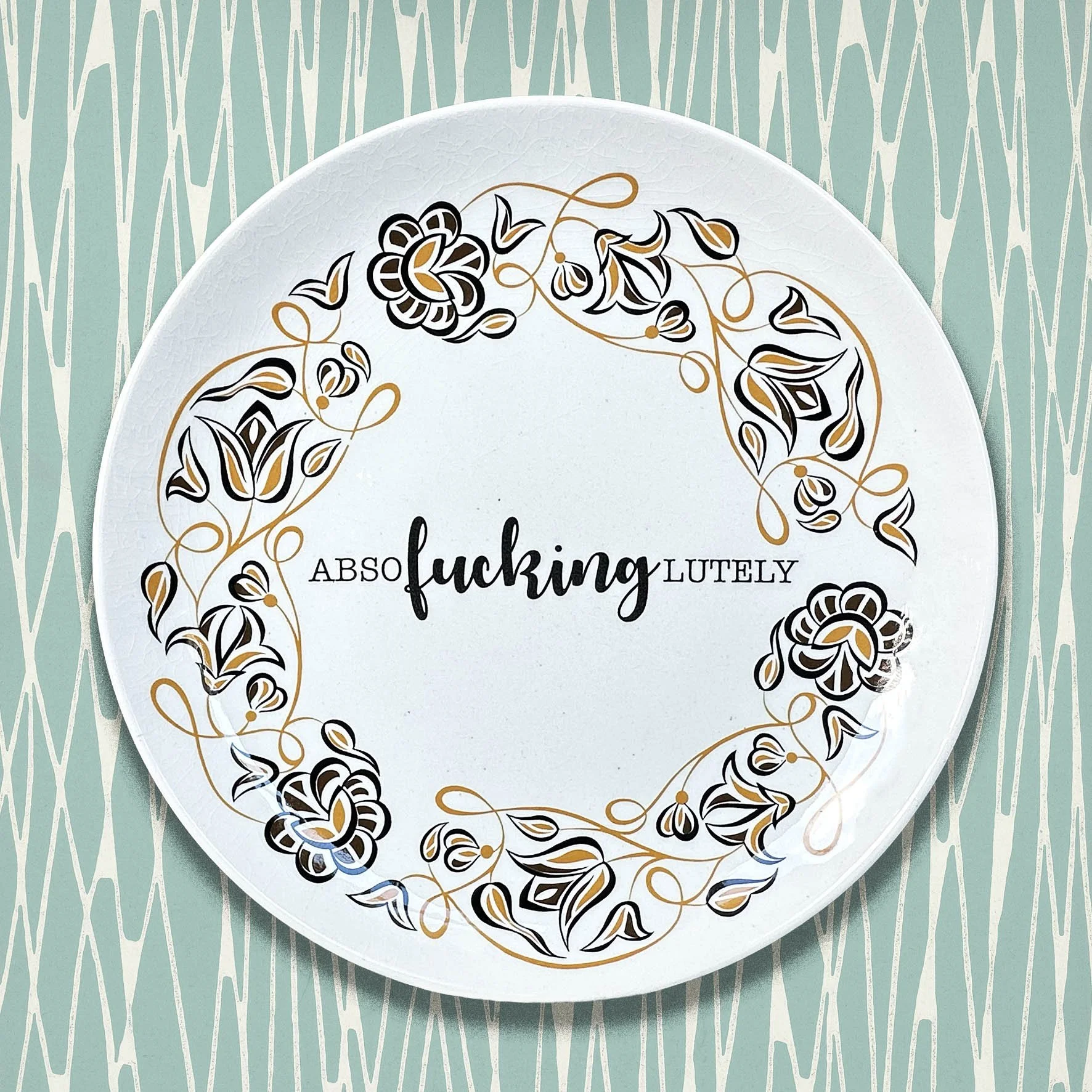 A vintage Poole plate with a black and mustard floral design and the word “absofuckinglutely”