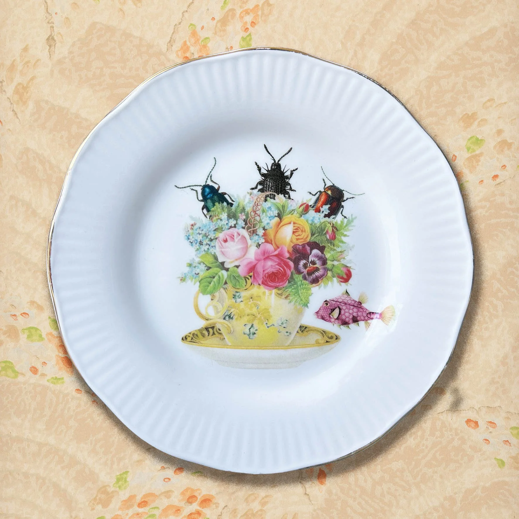 A vintage decorative plate with a picture of a tea cup full of flowers with bugs crawling out