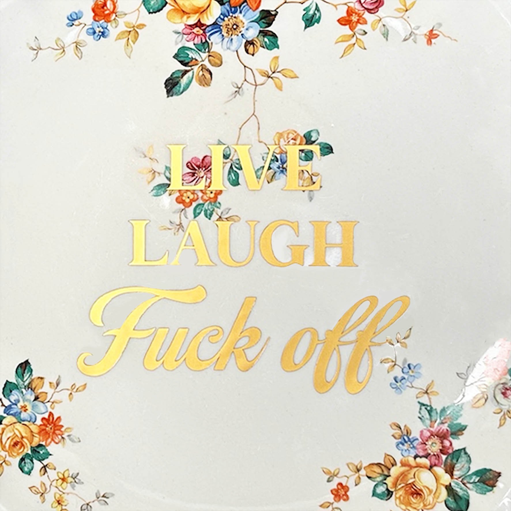 A vintage plate with a yellow, orange and red floral design with the words “live laugh fuck off” in gold writing