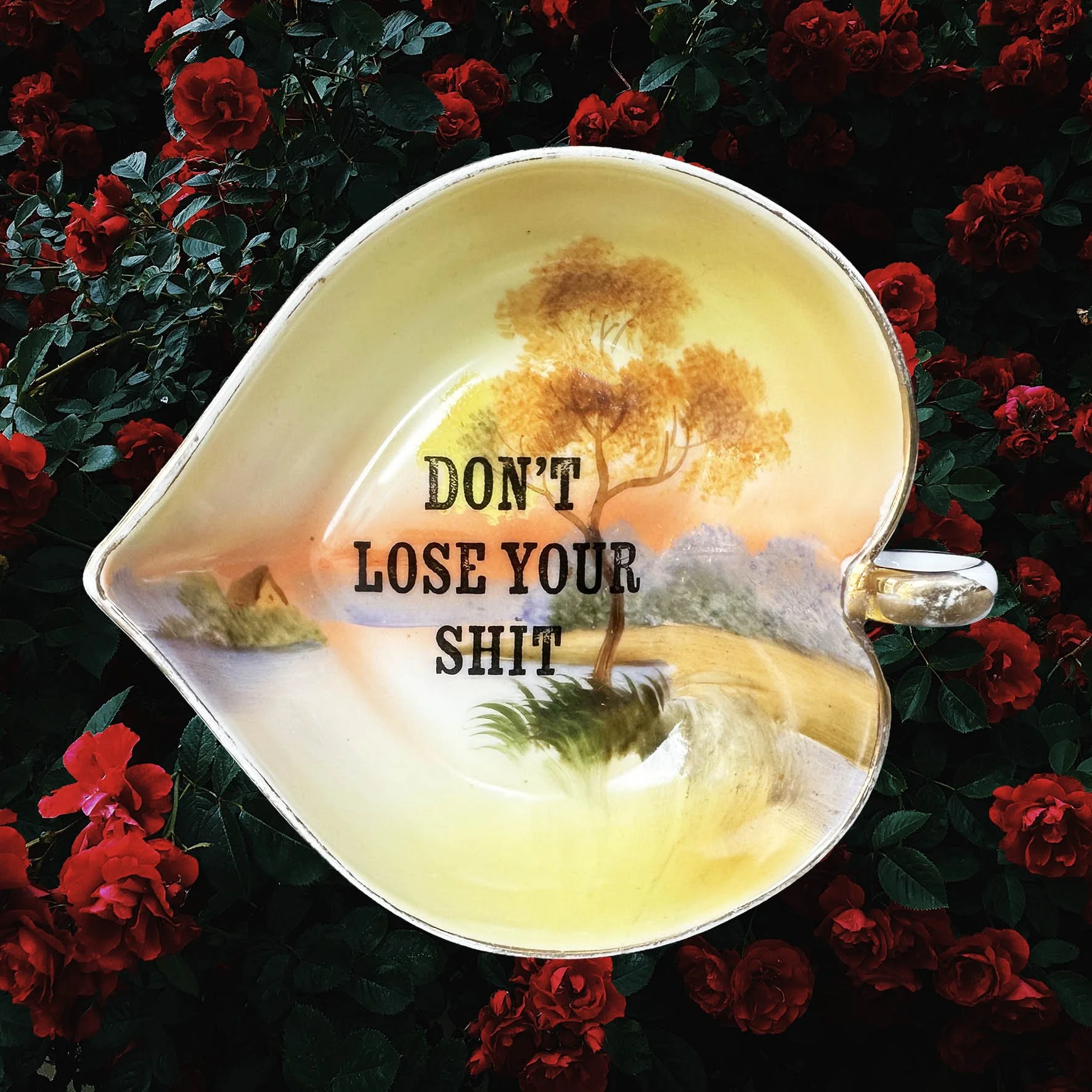 A heart shaped trinket dish with an orange, green and brown landscape design and the words “don’t lose your shit”