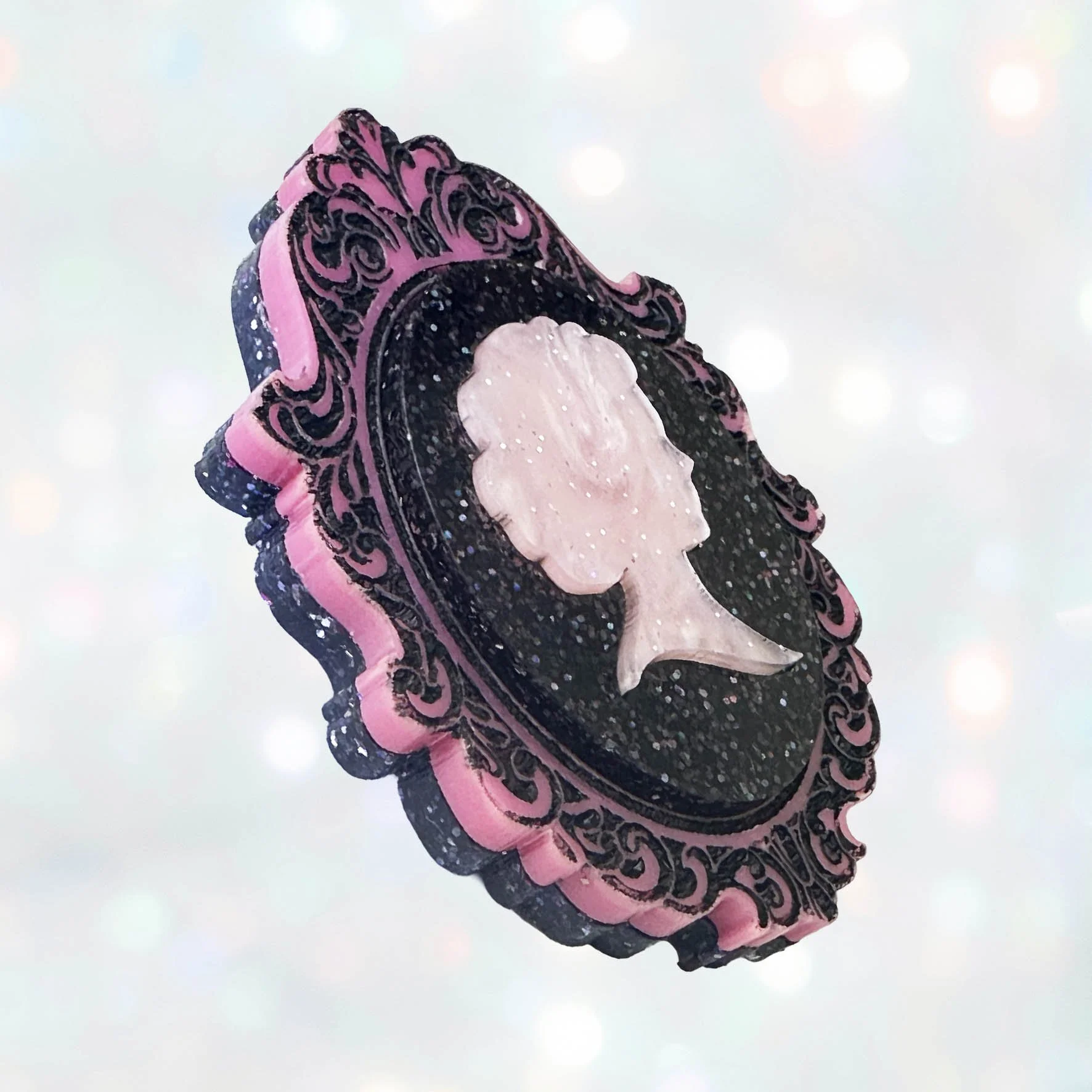 A pink and black glitter acrylic cameo style brooch featuring a silhouette
