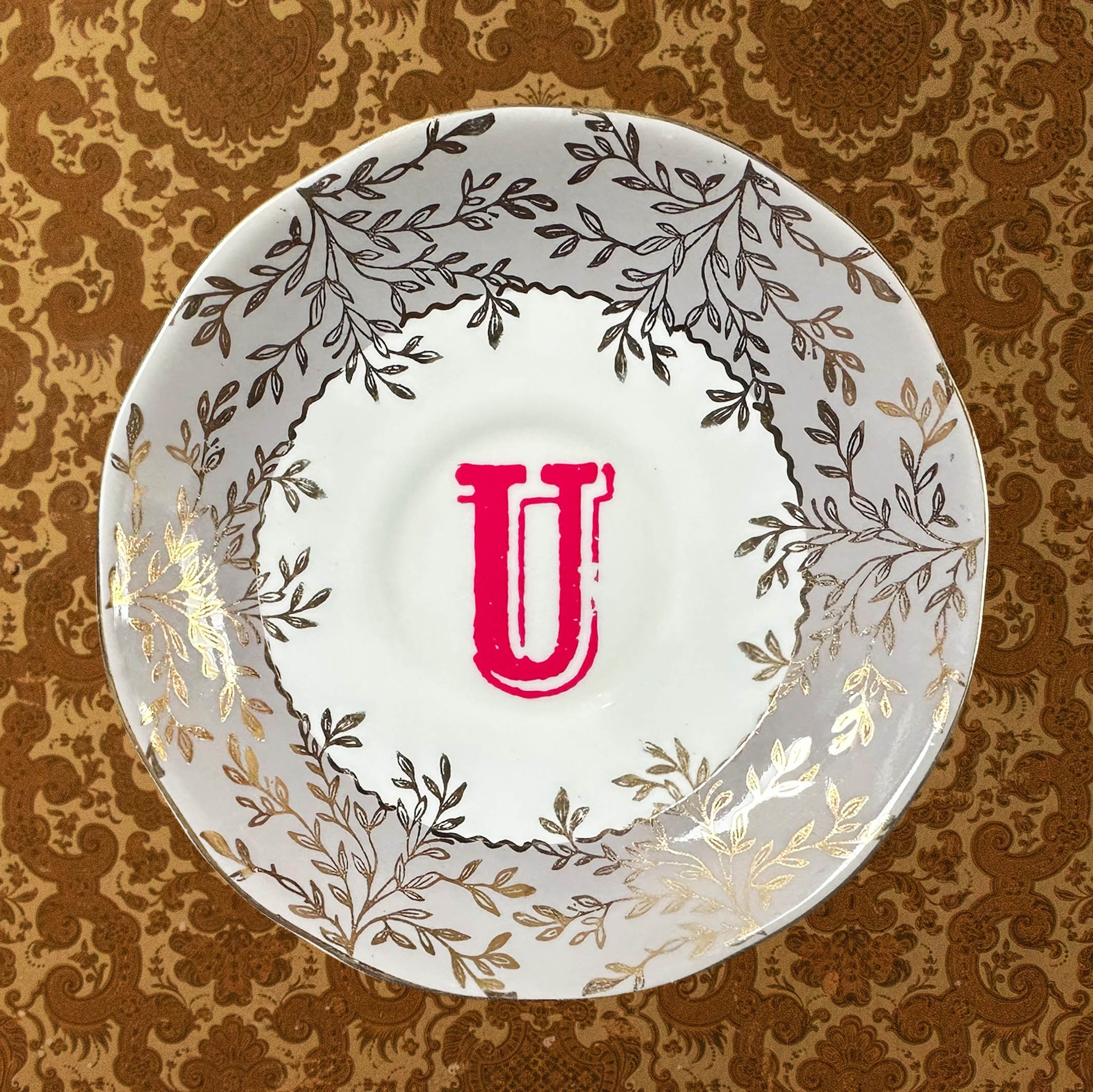Saucer 2 with the letter U in pink on a grey floral saucer