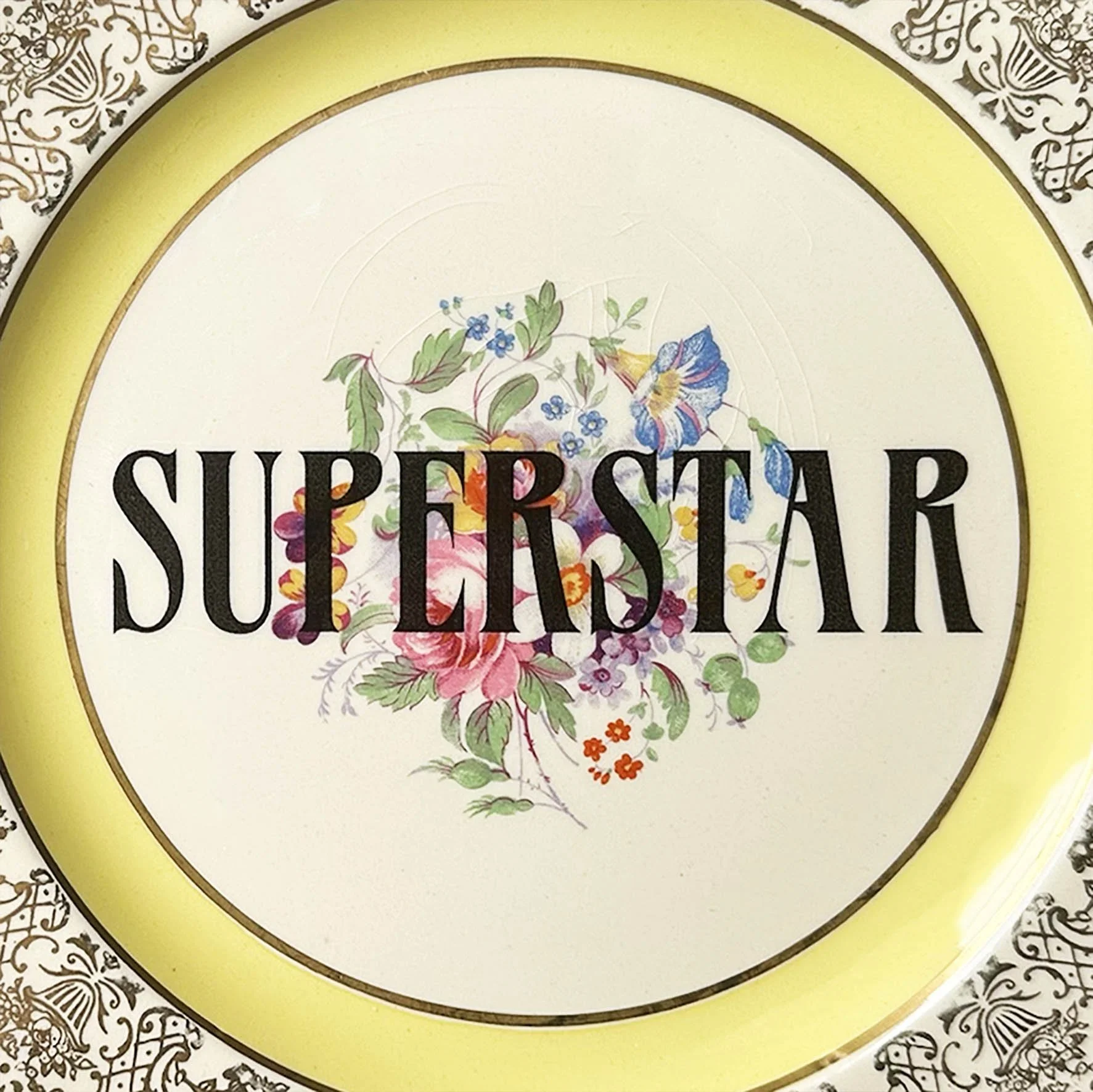 A vintage plate with a gold floral and yellow border and the word "superstar" in black lettering