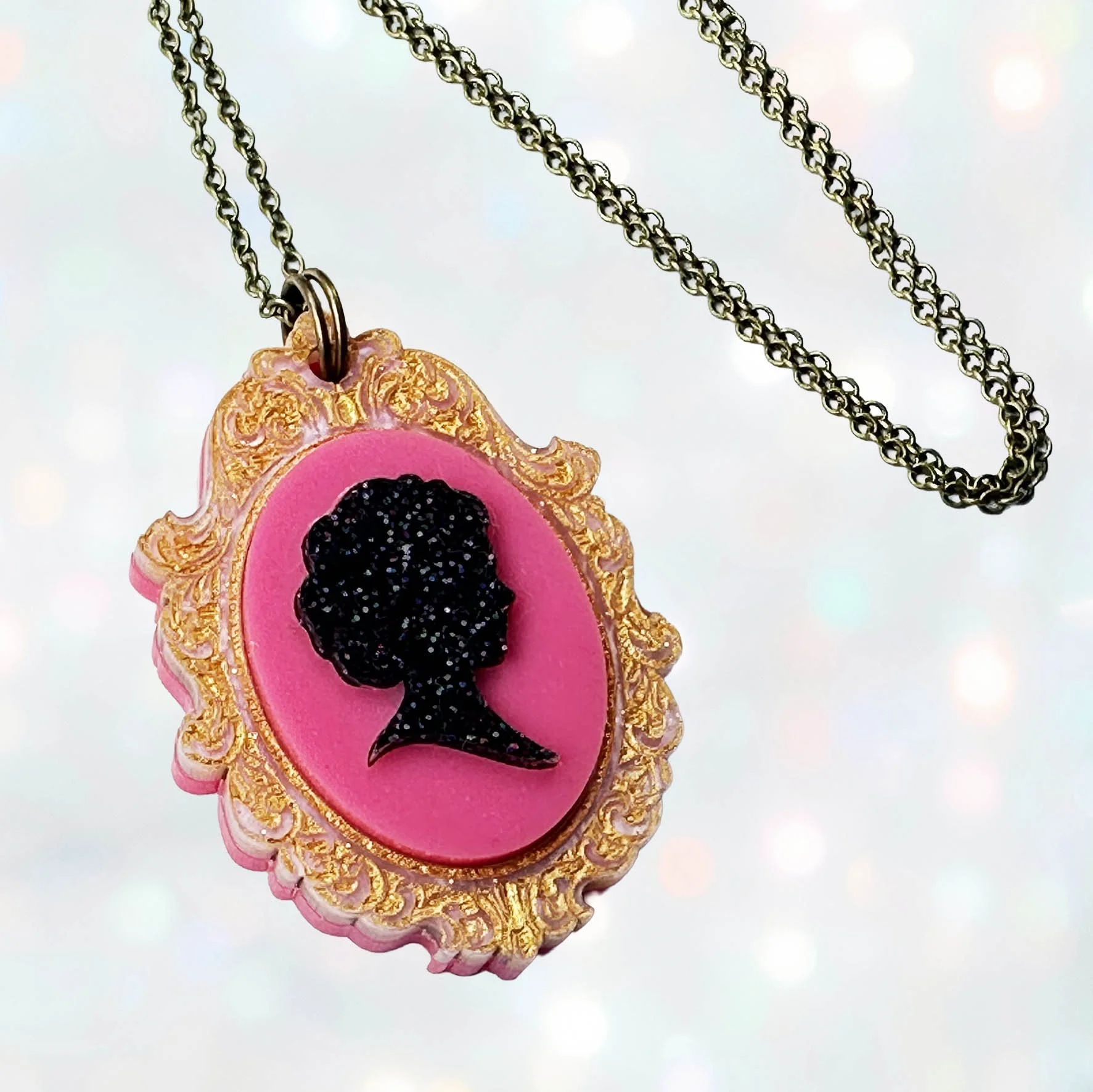 A pink, gold and black glitter laser cut acrylic cameo style necklace featuring a silhouette