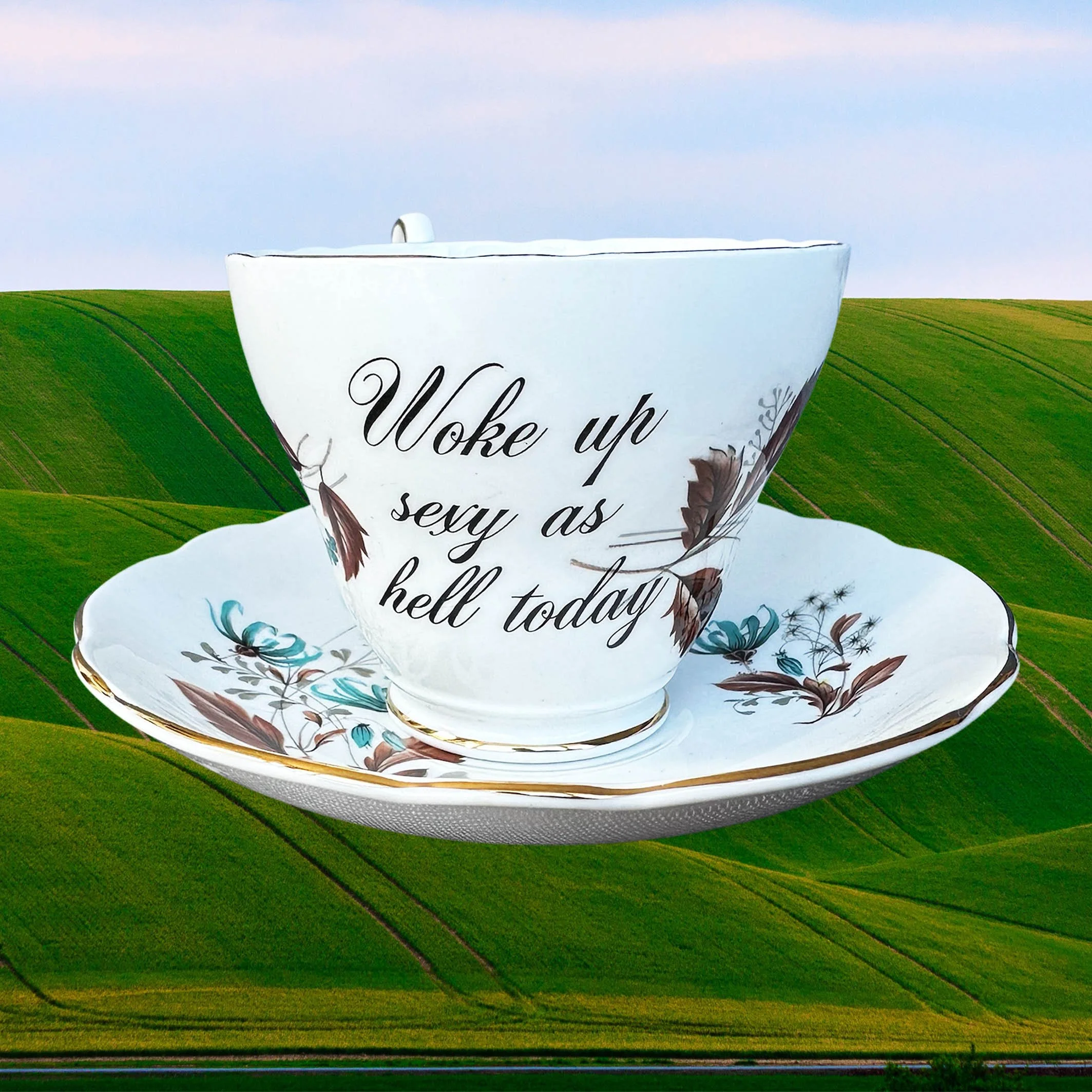 A vintage tea cup and saucer set with a blue and brown floral design, the words “woke up sexy as hell today” in black cursive writing