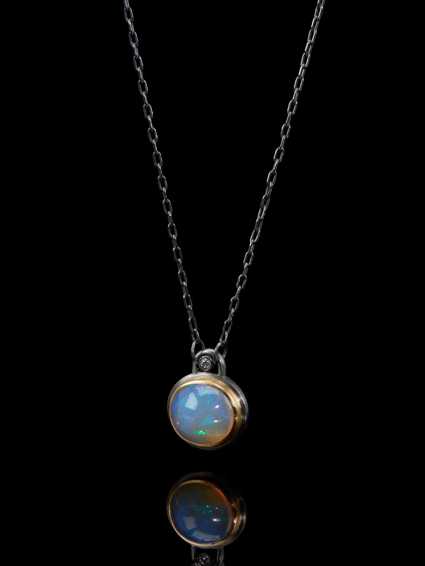 A luminous Ethiopian opal, its colour shifting with the light, set in 18ct gold and framed by oxidised silver.Designed as a small object to hold and wear, softly rounded and tactile, with a single diamond above creating a point of light.

Rune &mdash