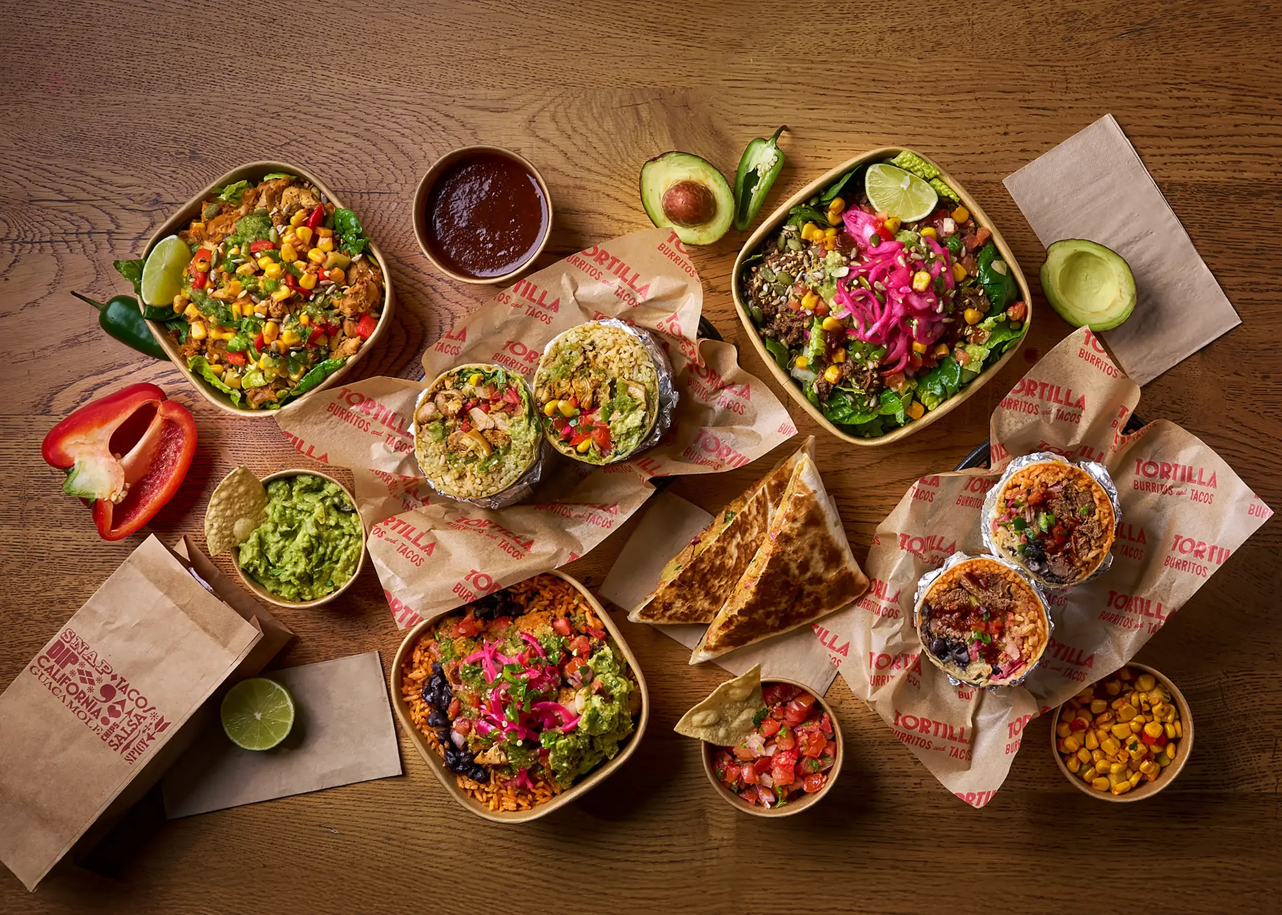 An array of Mexican food including tacos, burritos, rice, guacamole, salsa, and salads on a wooden table.