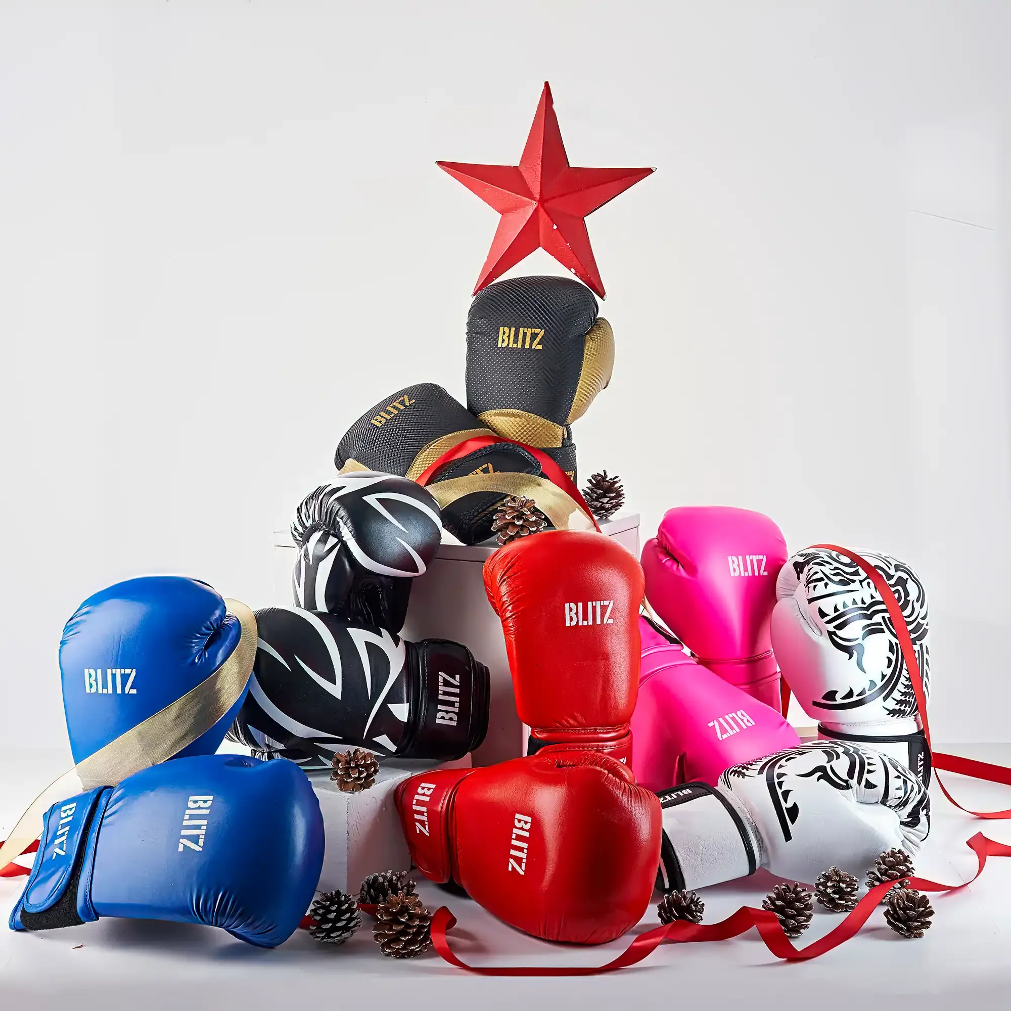 Boxing gloves in various colors such as red, blue, pink, black, and white, arranged on a white surface with pinecones and red ribbons, and a red star decoration at the top.