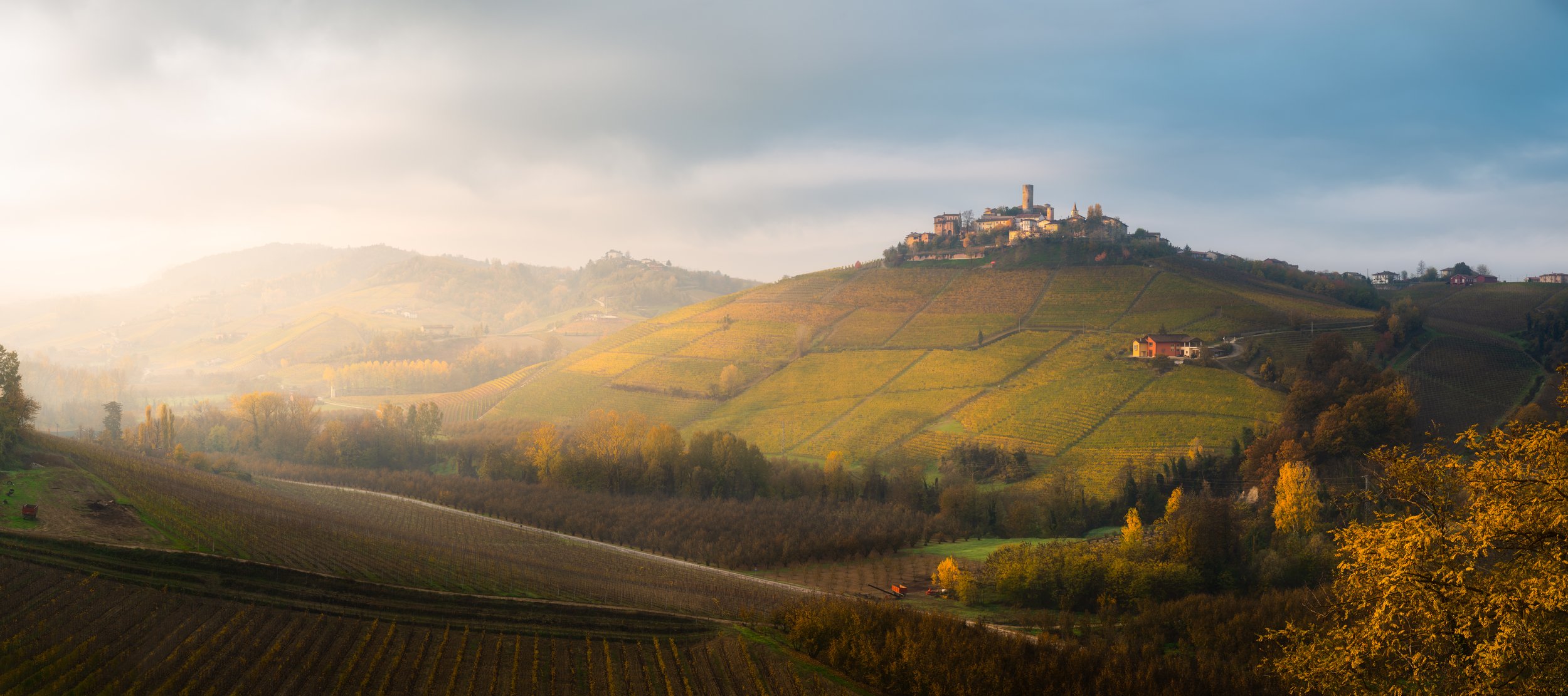 Paesaggio collinare con vigneti, alberi autunnali e un castello in cima a una collina