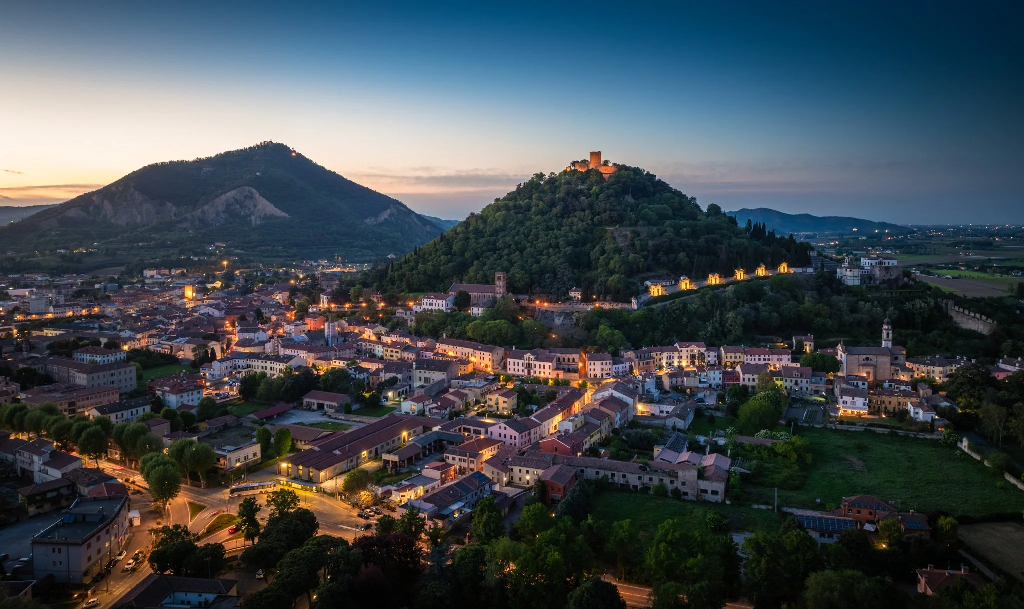 Panoramica della città di notte con colline e castelli illuminati.