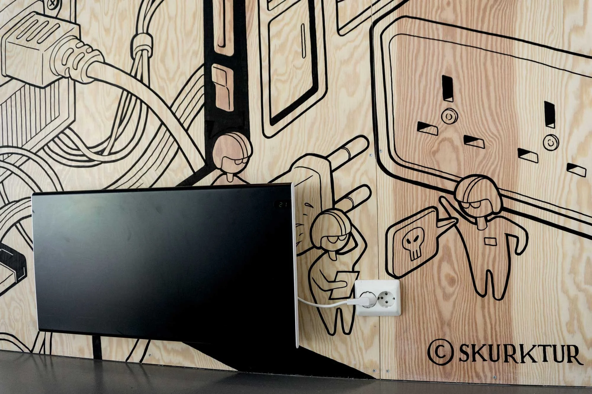 Wall mural depicting stylized line drawings of children with headphones, electrical outlets, and electronic devices, with a monitor in front. 