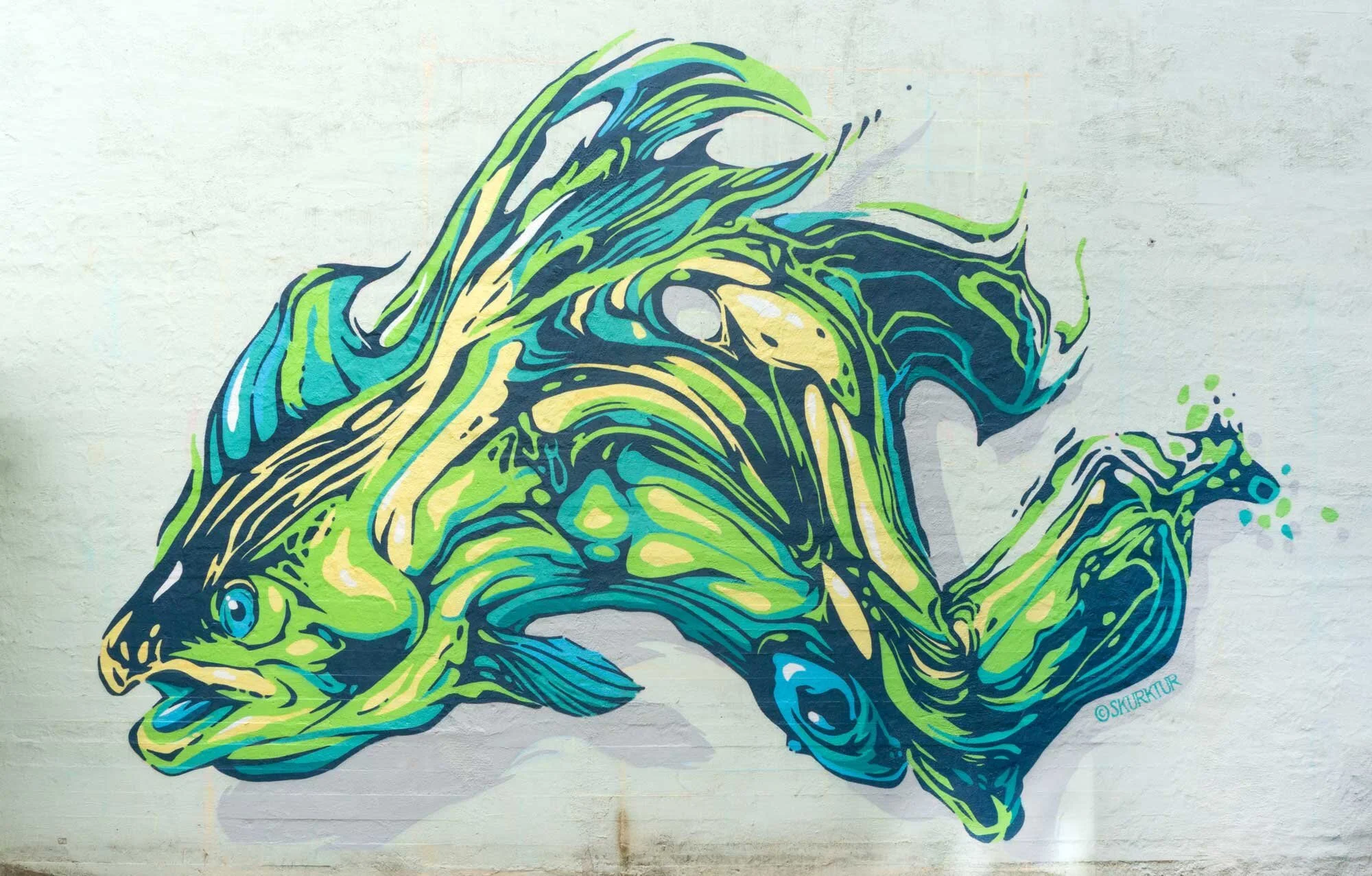 Colorful graffiti mural of a fish painted on a brick wall, featuring shades of green, blue, and black with detailed lines and splashes of color.