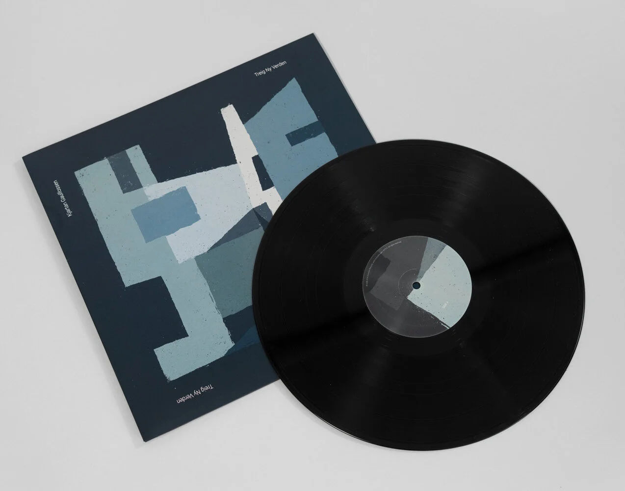 A vinyl record partially removed from its album cover on a white surface. The cover features an abstract, geometric design in shades of blue and white.