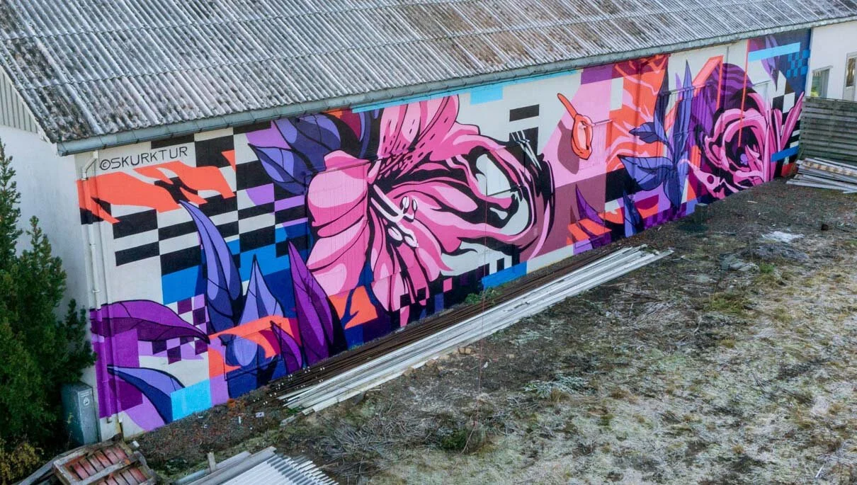 Colorful mural of pink and purple flowers with abstract geometric background on the side of a building.