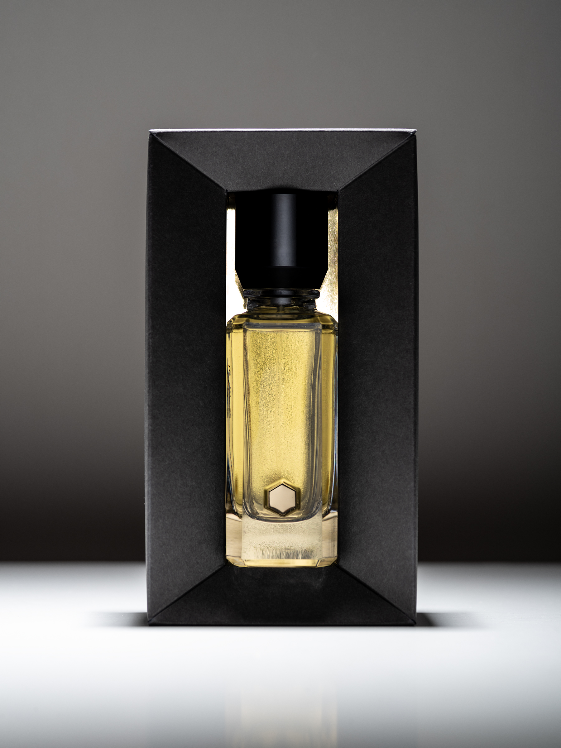 Glass perfume bottle with yellow liquid and black cap in a black box. — D:SOL