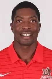 Person wearing a brown polo shirt with a logo, smiling and having braided hair.