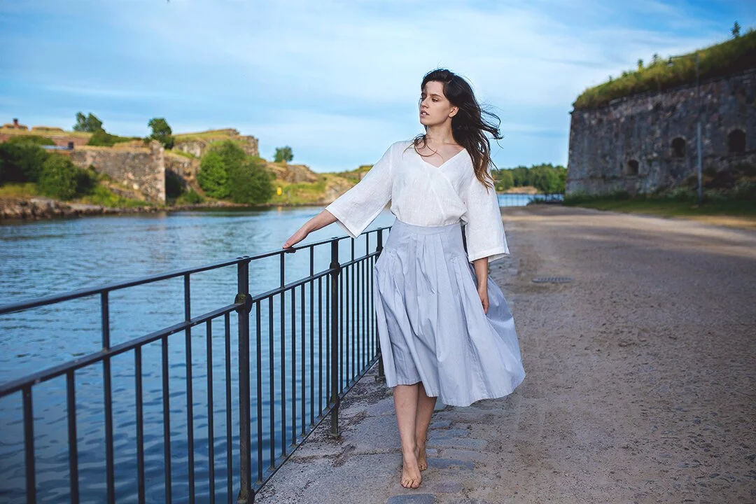 Valoisa ja ilmava henkilökuvaus ulkona – nainen kävelemässä valkoisessa mekossa kesäpäivänä.