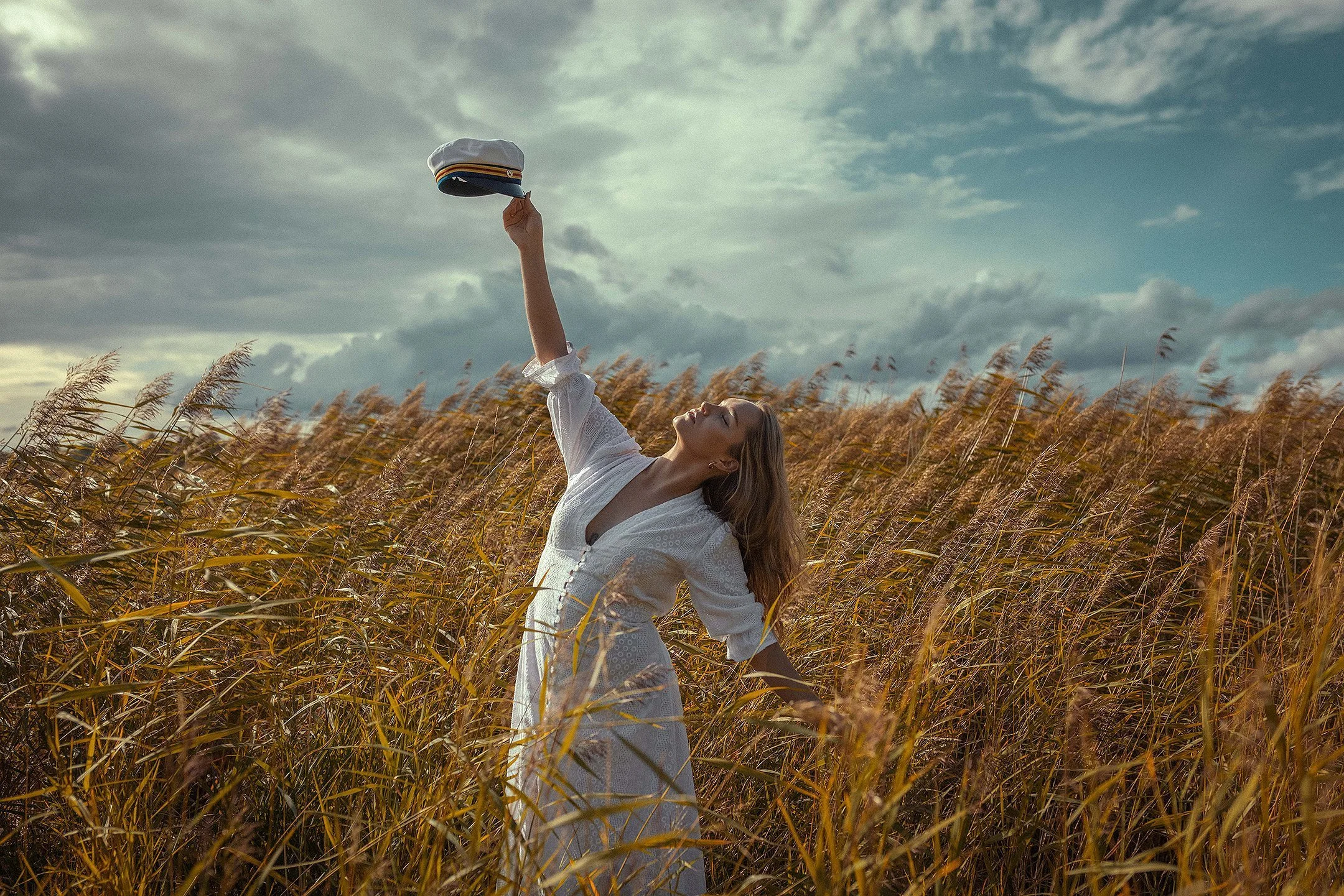 Iloinen ylioppilaskuvaus miljöössä – vastavalmistunut nainen heiluttaa ylioppilaslakkia viljapellon keskellä.