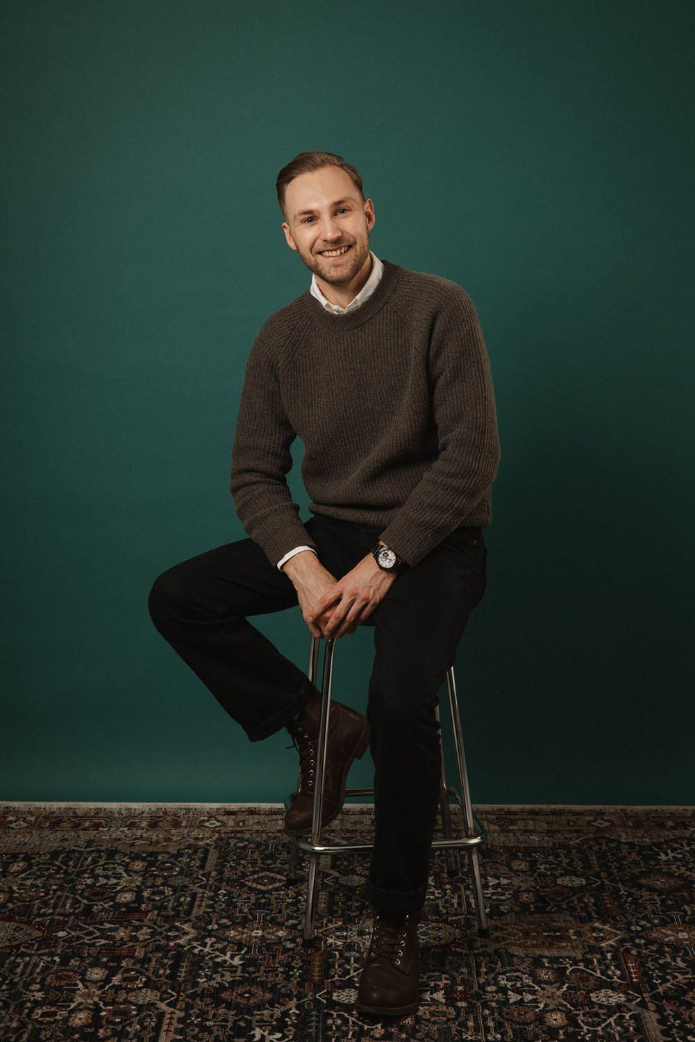 Ammattimainen henkilökuvaus studiossa – mies istuu rennosti korkealla tuolilla vihreää taustaa vasten.