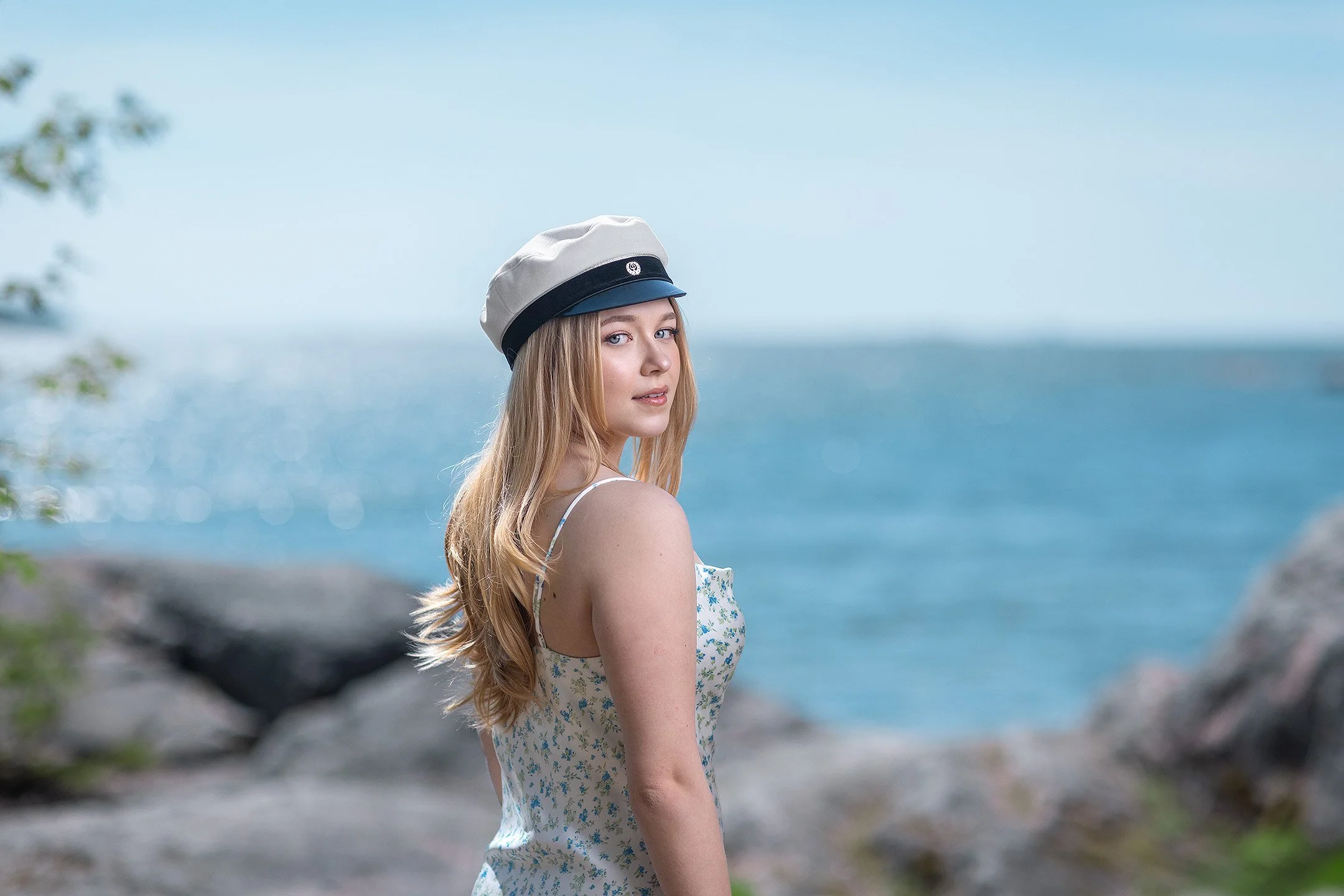Klassinen ylioppilaskuvaus meren rannalla – ylioppilaslakki päässä oleva nainen poseeraa kallioisessa saaristomaisemassa.