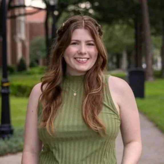 headshot of emily mcmahon-lynch in an outdoor setting, facing the camera, smiling, wearing a green top