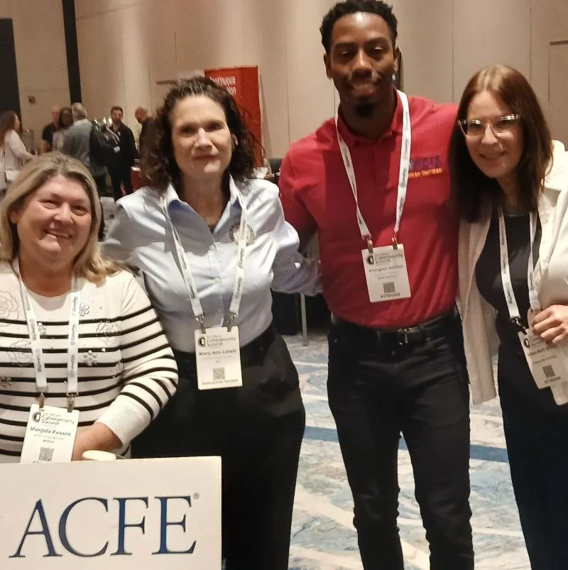 Elissa and three other people standing together, in a conference room, smiling, with name tags around their necks and a sign that reads 'ACFE' in front of them.