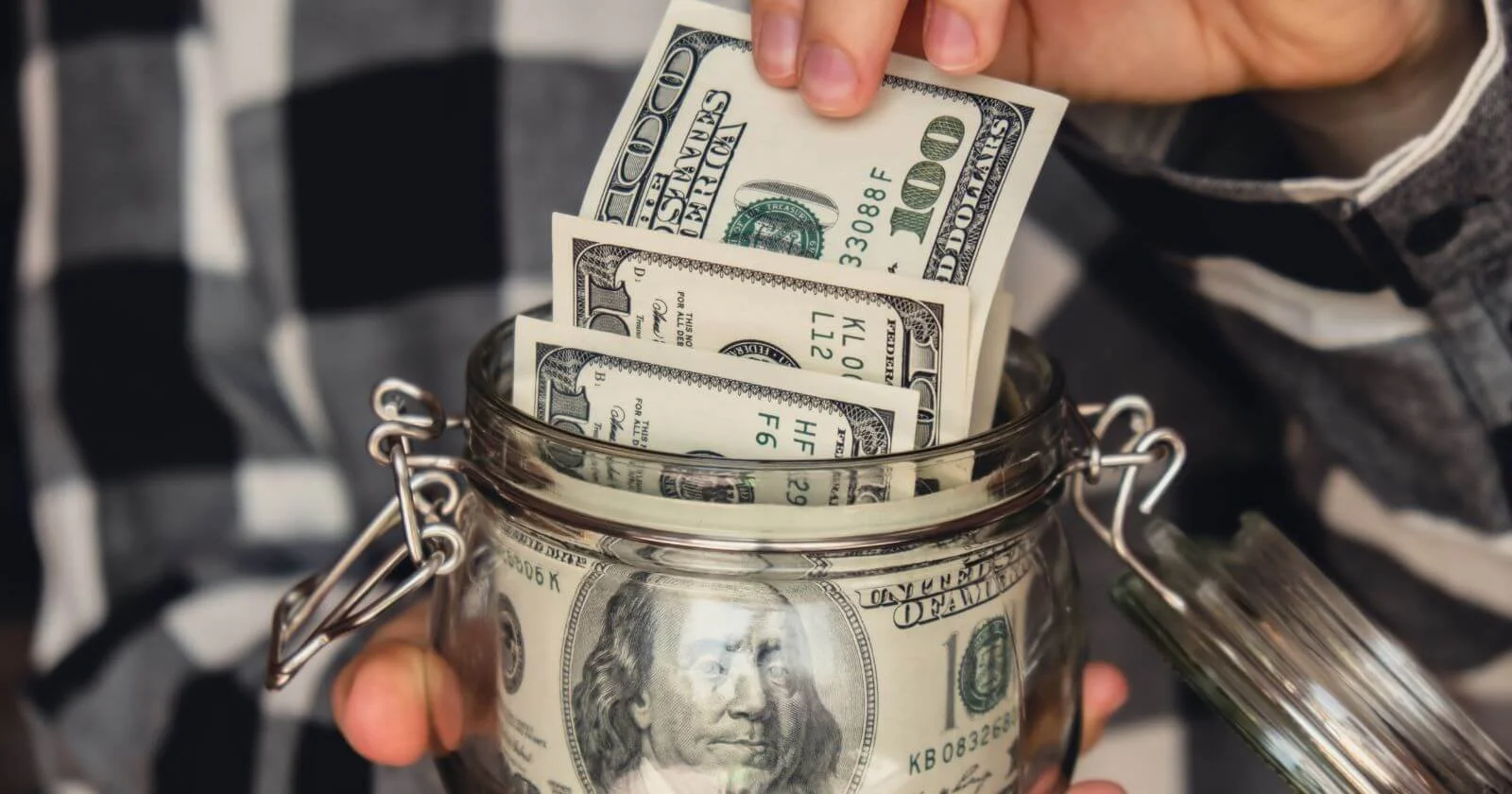 Aspiring business owner pulls $100 bills out of a jar considering the costs of starting a business.