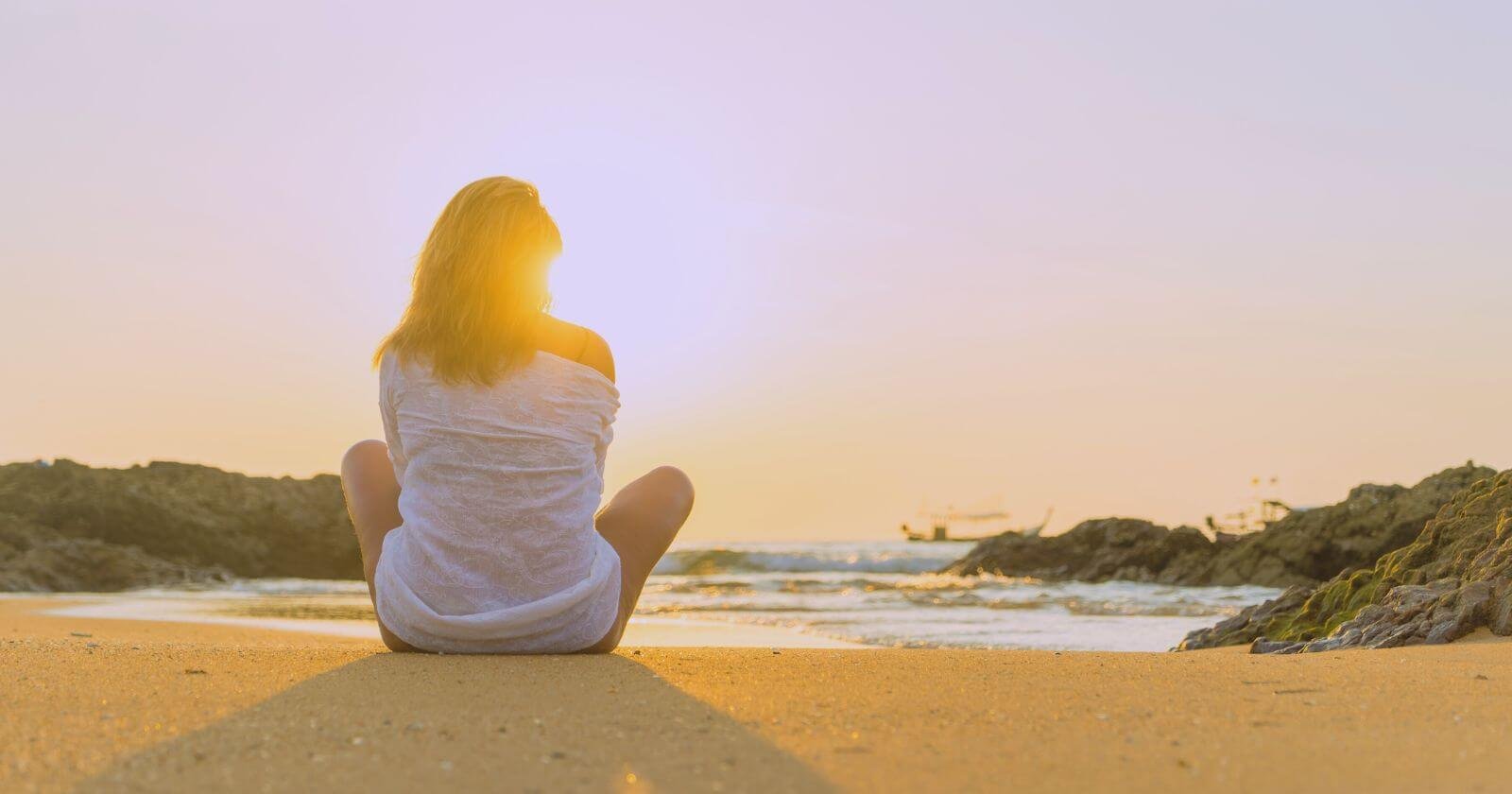 Woman sitting on sunny beach contemplating the purpose of life.