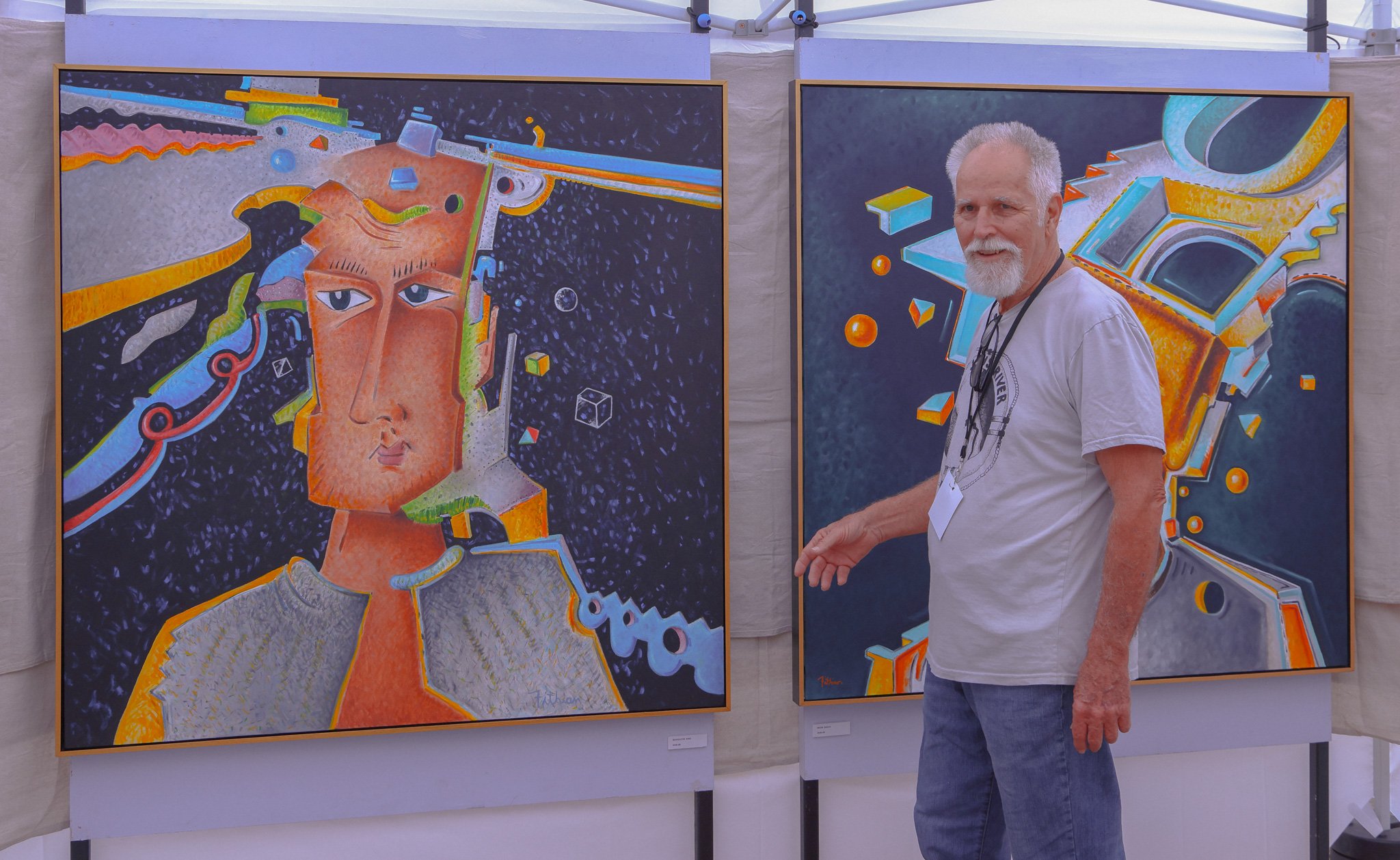 Photograph of the late artist David Fithian standing in a tent at the Fall Festival of the Arts - DeLand beside two of his large, vibrant, abstract paintings.