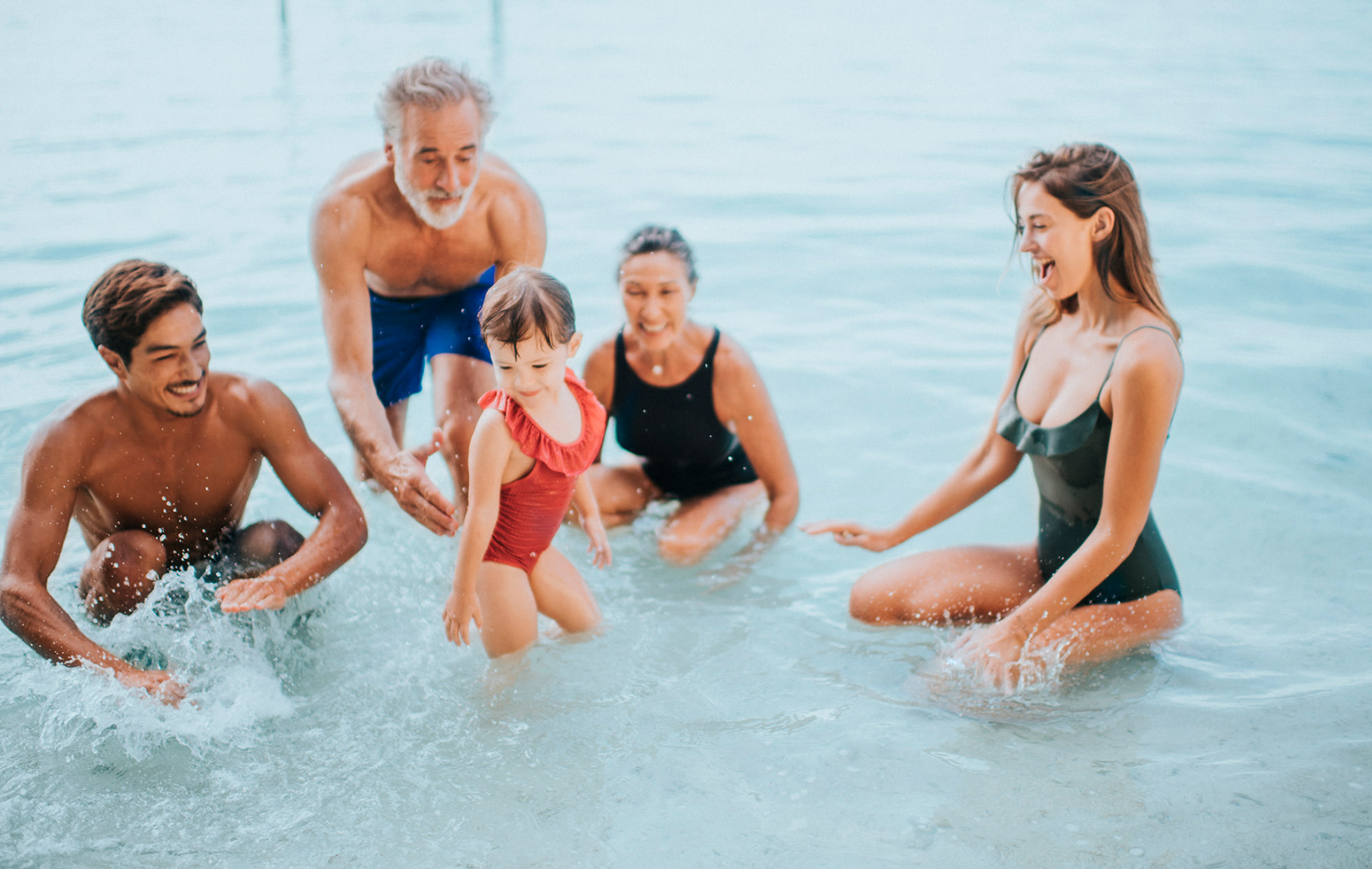 Four adults and a child in swimwear splashing in a pool for a Club Med campaign, with wardrobe styling by Molly McIntyre. Photographed by Catherine Falls.
