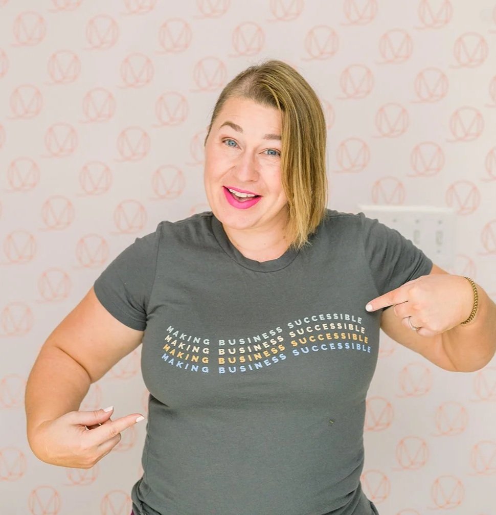 Erin is smiling and pointing at her shirt that says Making Business Successible.