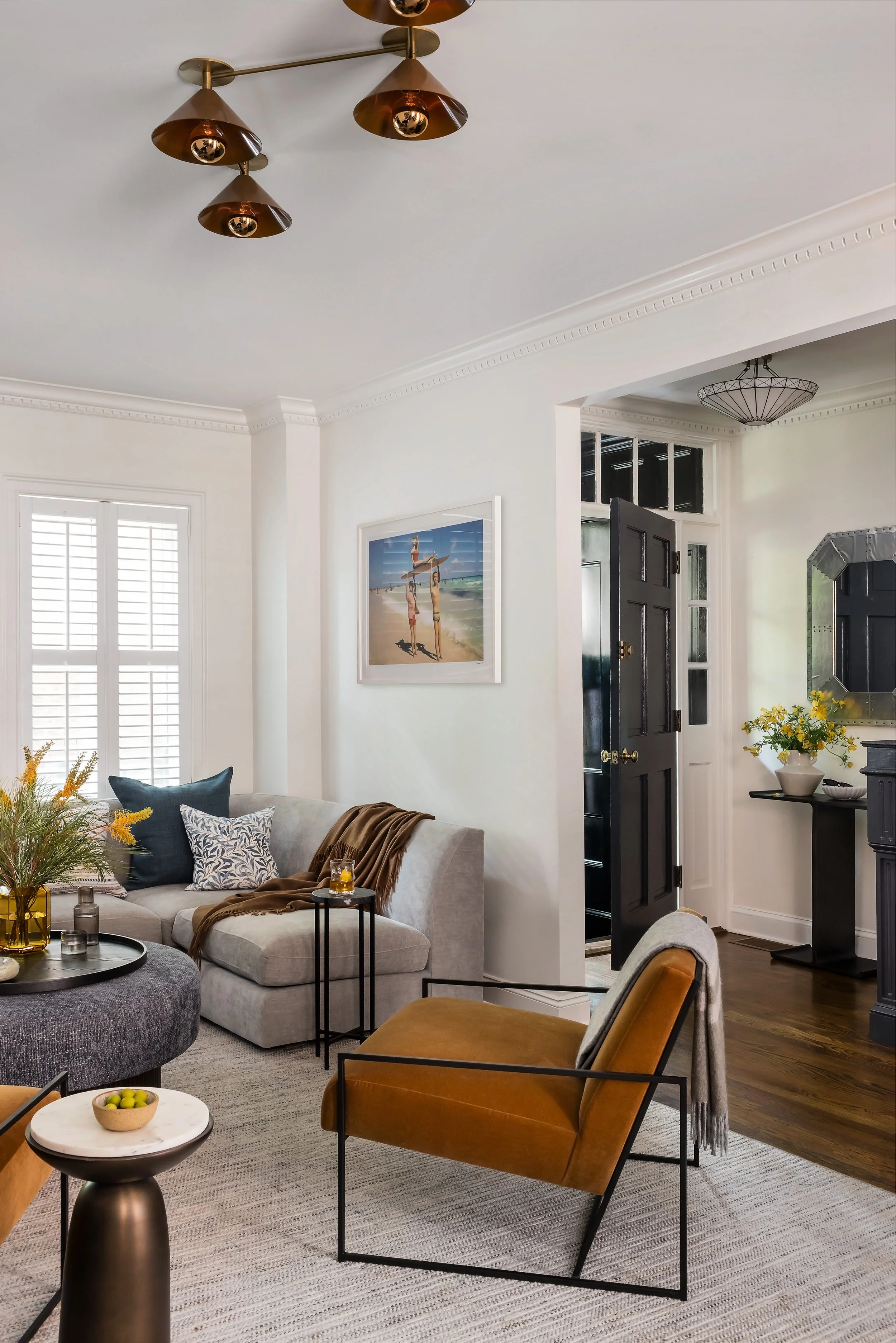 Living room sectional with a framed beach photograph, opening into an entry hallway with a black front door and vintage mirror.