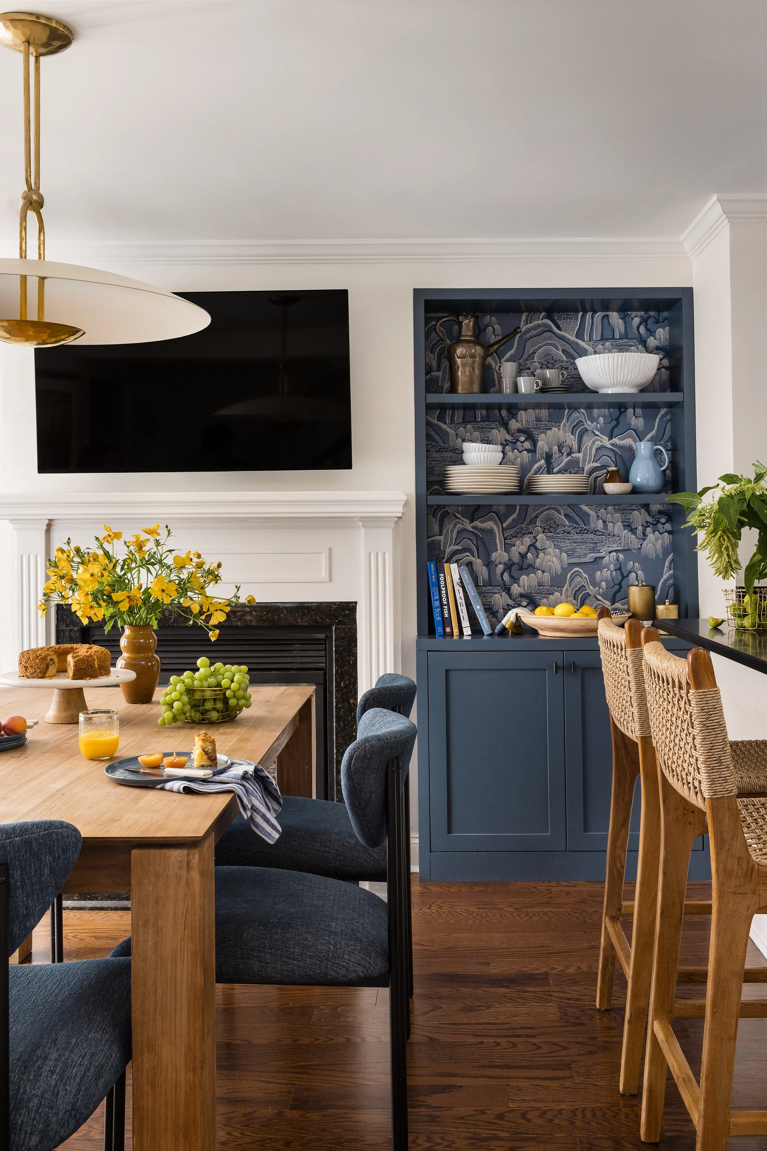 Close-up of a navy built-in hutch with chinoiserie wallpaper backing, ceramic dishware, and a breakfast spread on the table below.