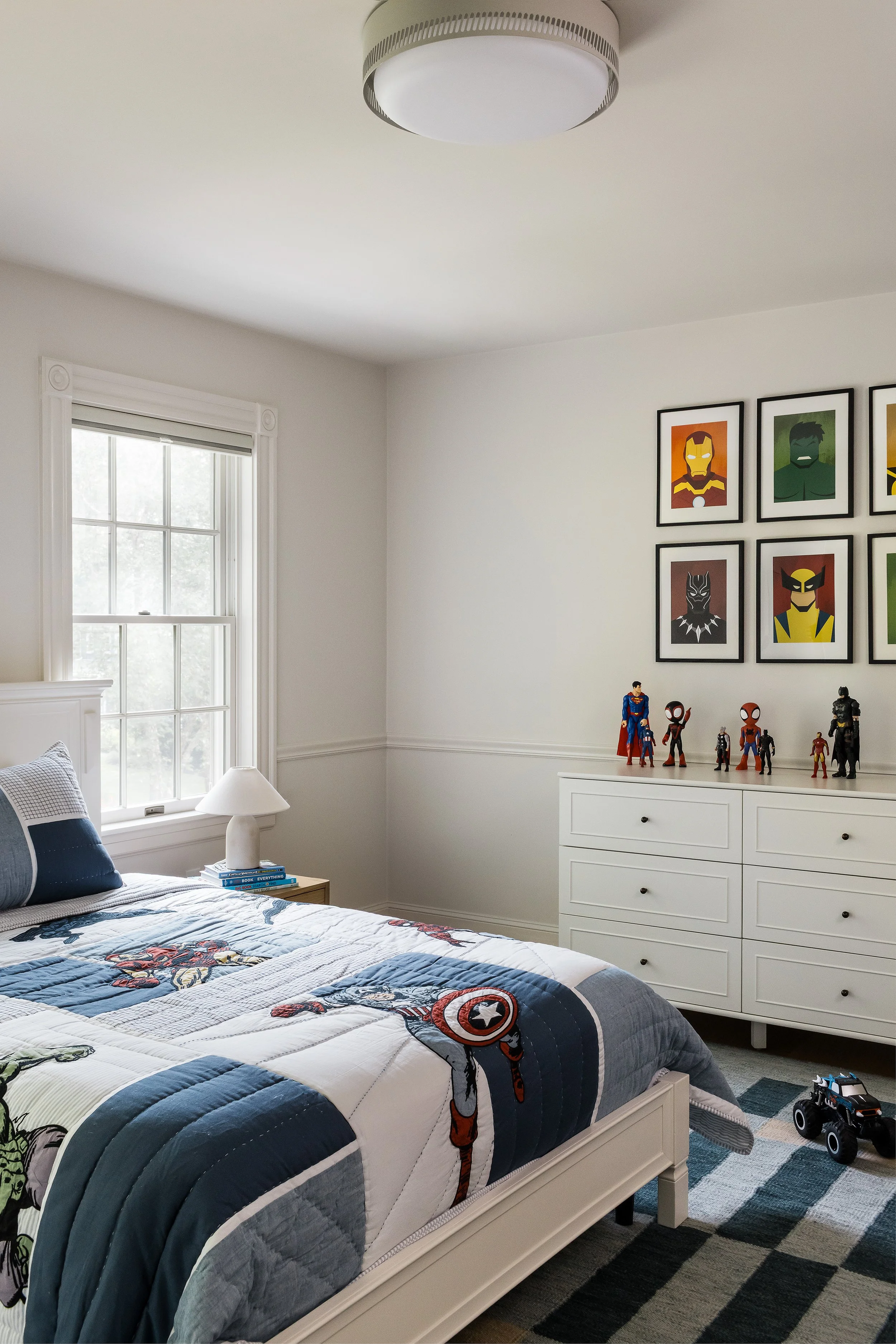 Boy's bedroom with a superhero quilt, a gallery of framed Marvel character prints, and action figures displayed on a white dresser.
