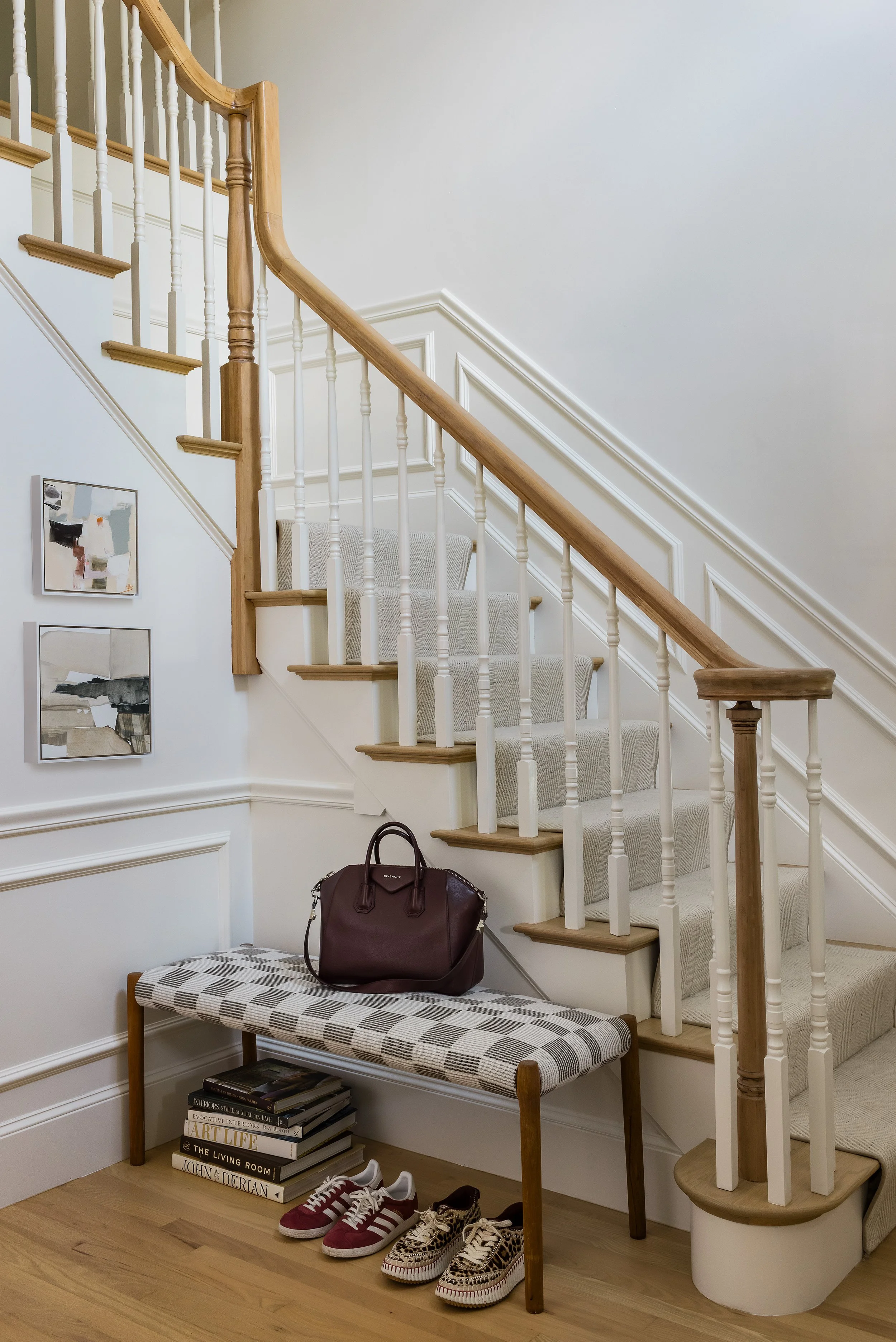 Wood and painted staircase with a checked bench, stacked design books, and a leather handbag at the base.