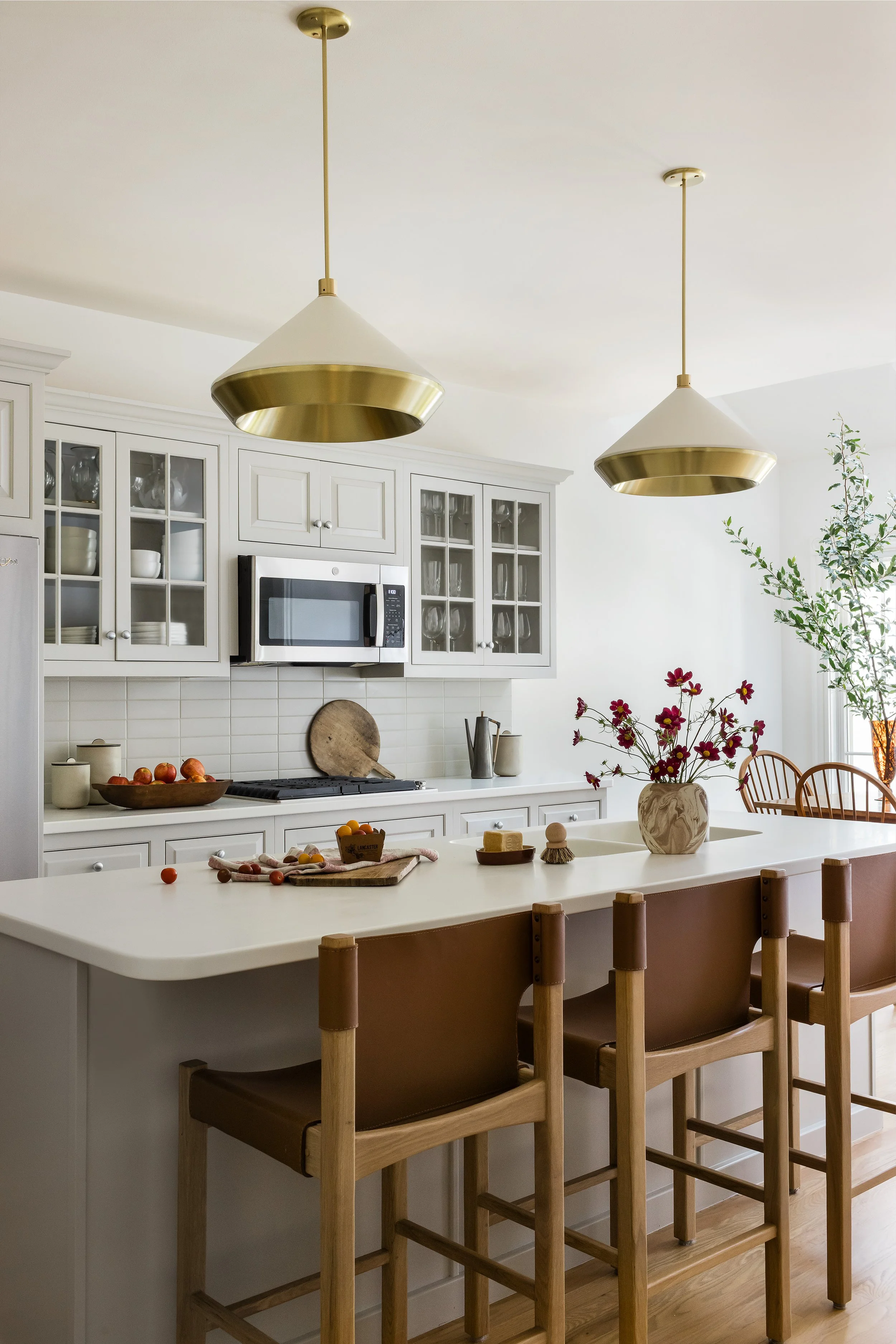 Kitchen with white cabinetry, brass and cream pendant lights over an island, and leather counter stools.
