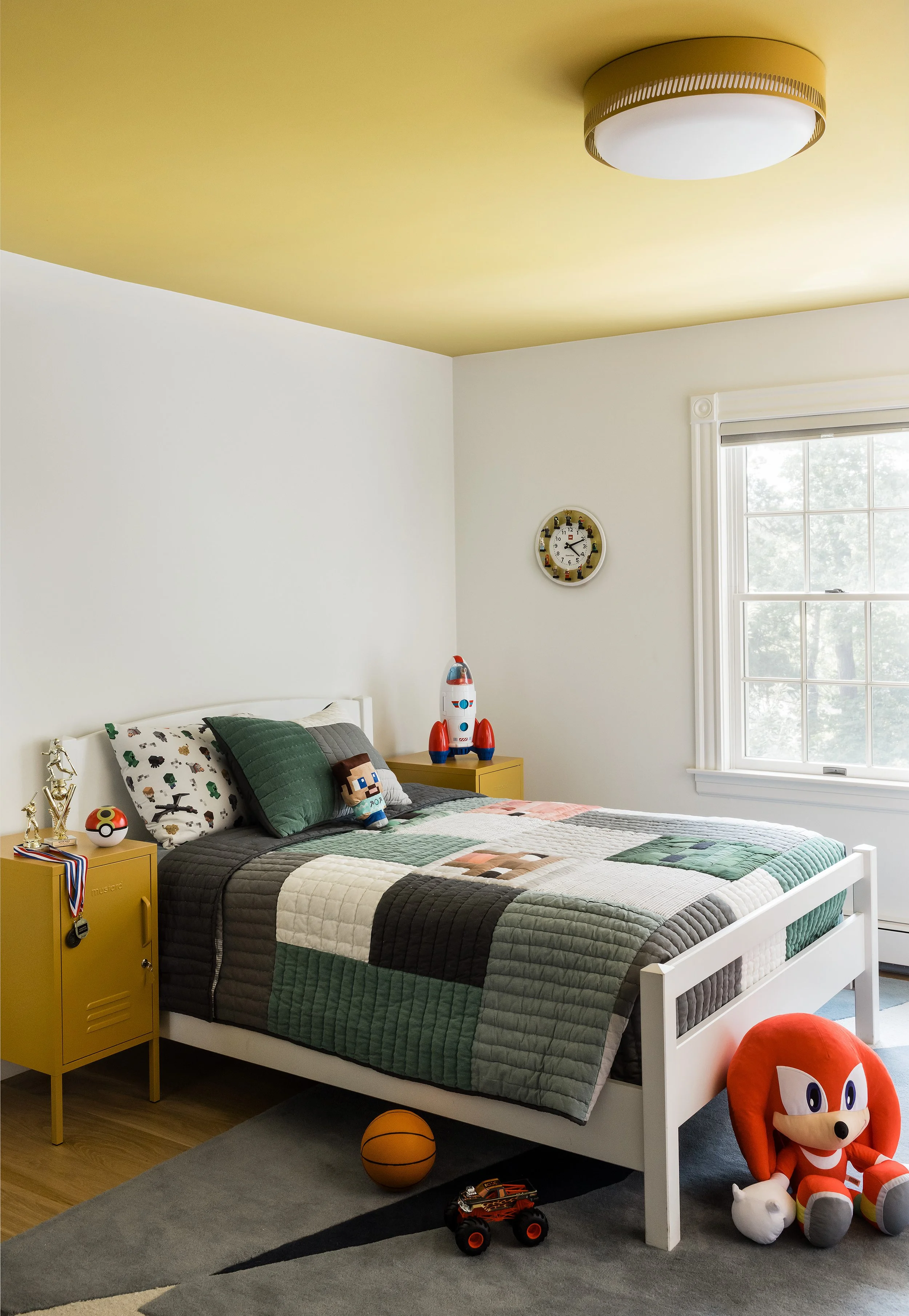 Boy's bedroom with a yellow painted ceiling, gray and white patchwork quilt, and a mustard locker-style nightstand.