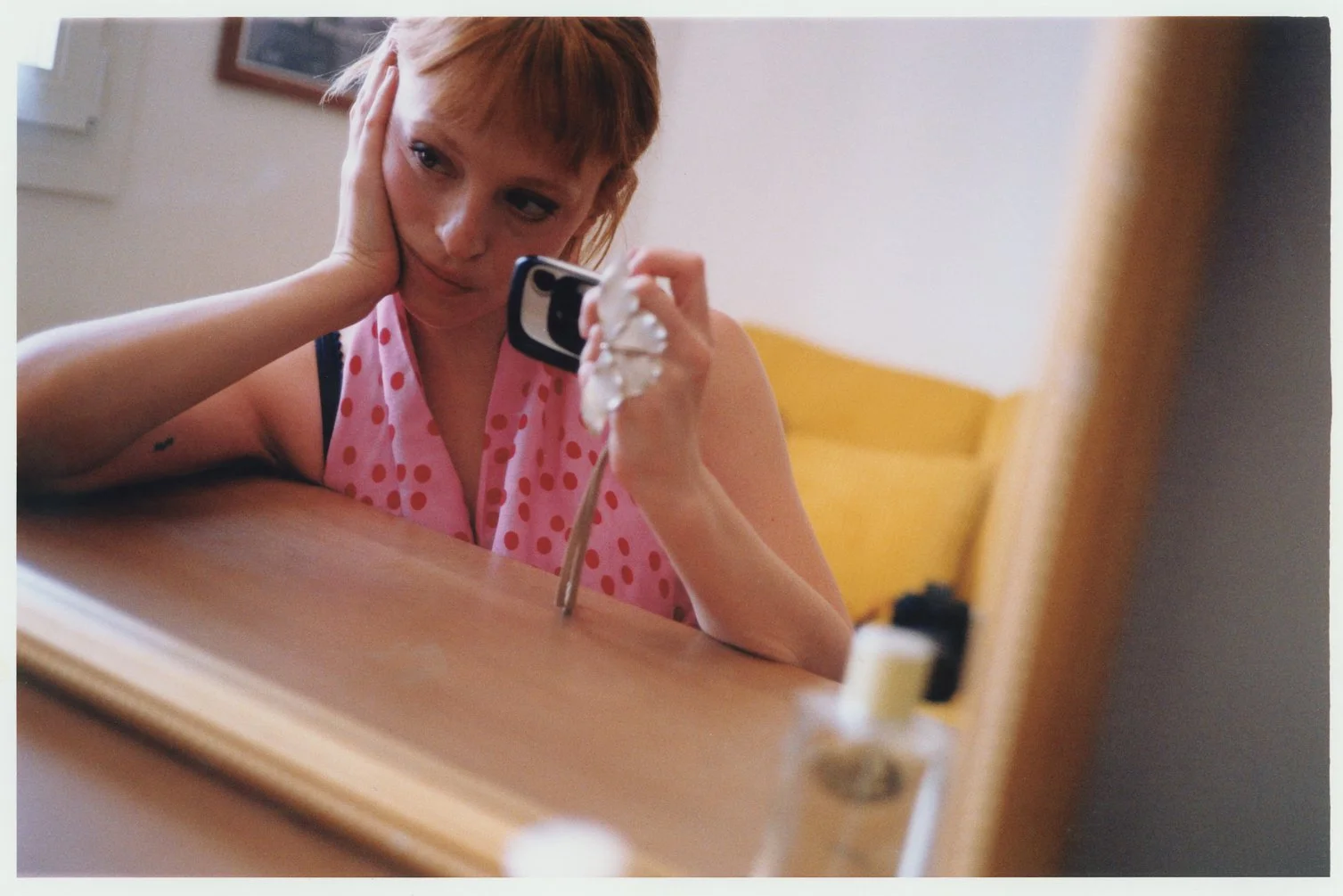 Catalina looking in the mirror, leaning on her hand on her cheek, with a digital camera