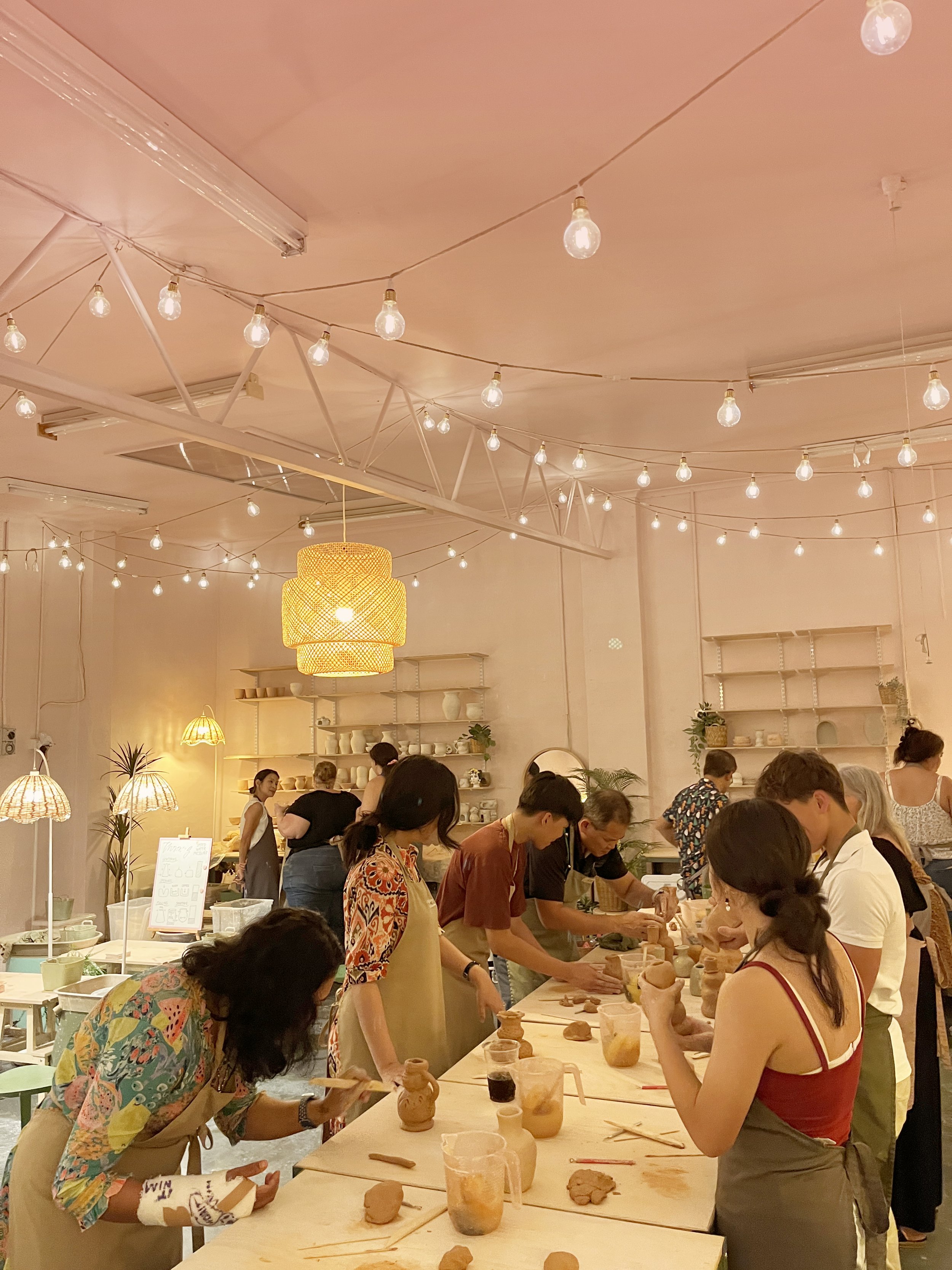 People engaged in pottery class under decorative hanging lights.