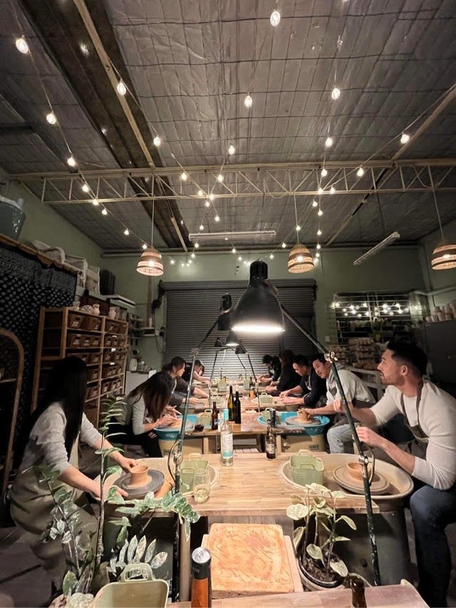 Group pottery class in a workshop with hanging lights and plants