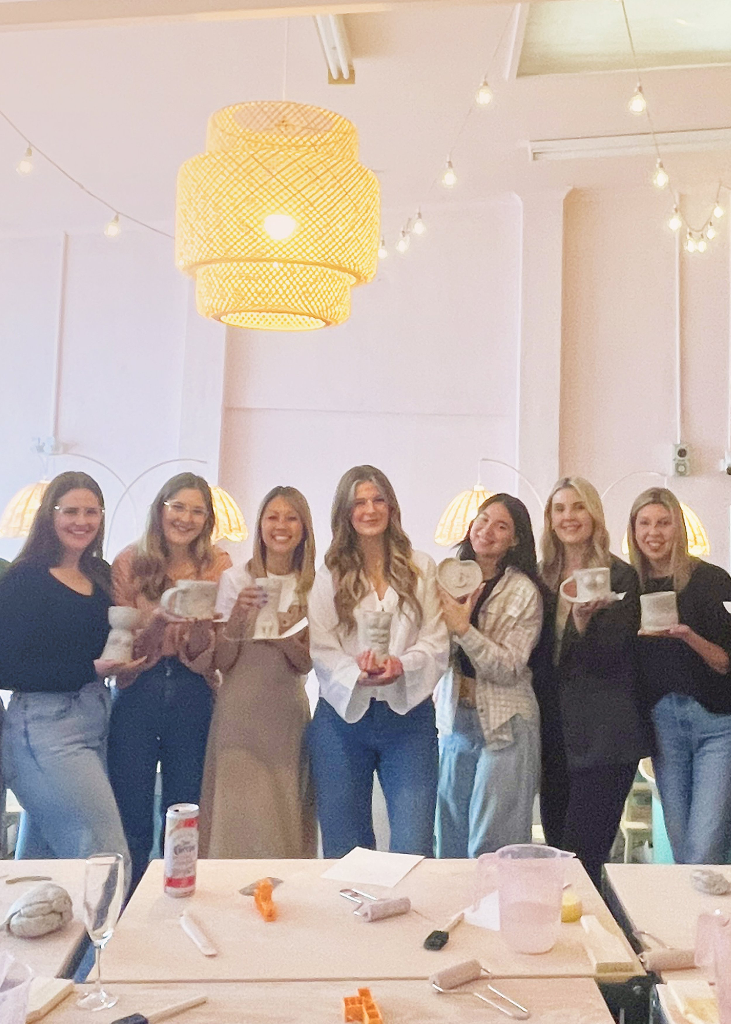 Group of women holding pottery in a room with soft lighting and ceiling lamps.