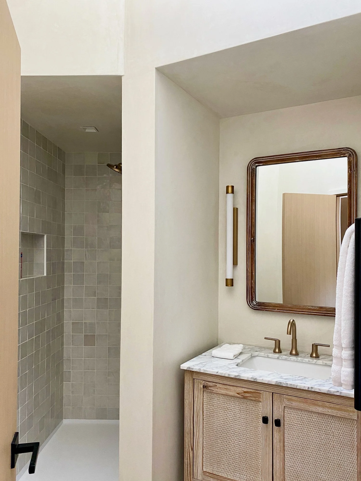 Bathroom with a walk-in shower with beige tiles and a wooden vanity with a marble countertop, mirror, and towels.