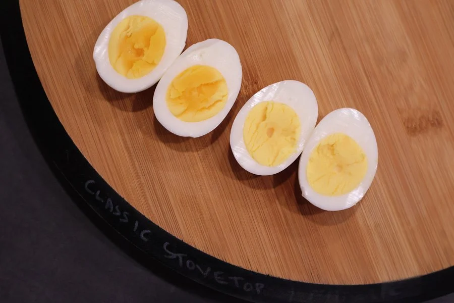 Four air fryer boiled eggs, sliced in half, are arranged on a round wooden cutting board.