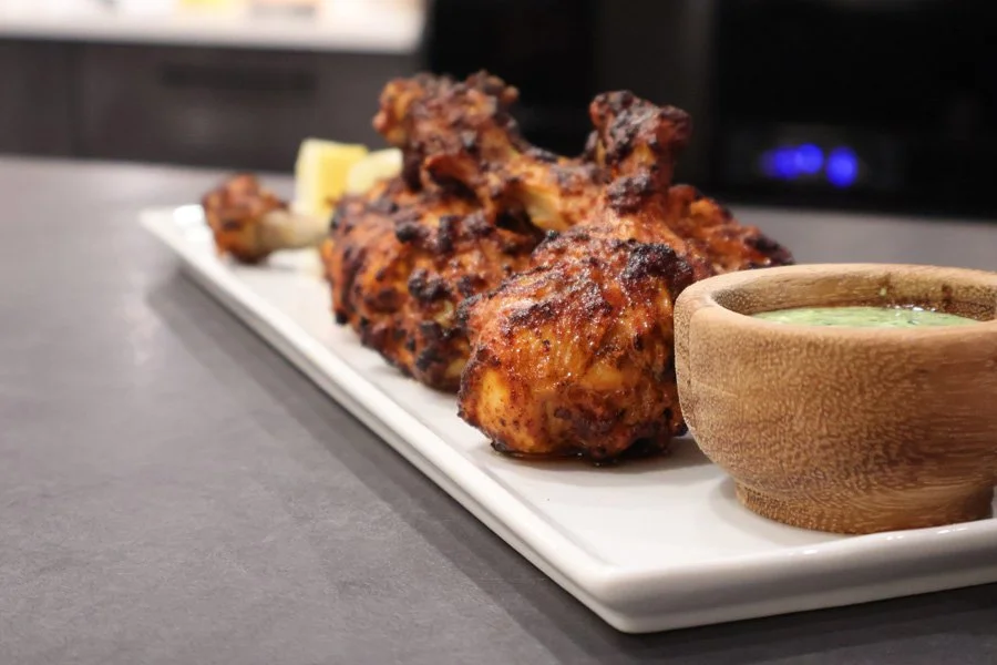 Air fryer tandoori chicken drumsticks on a white plate with a wooden bowl of green dipping sauce on the side.