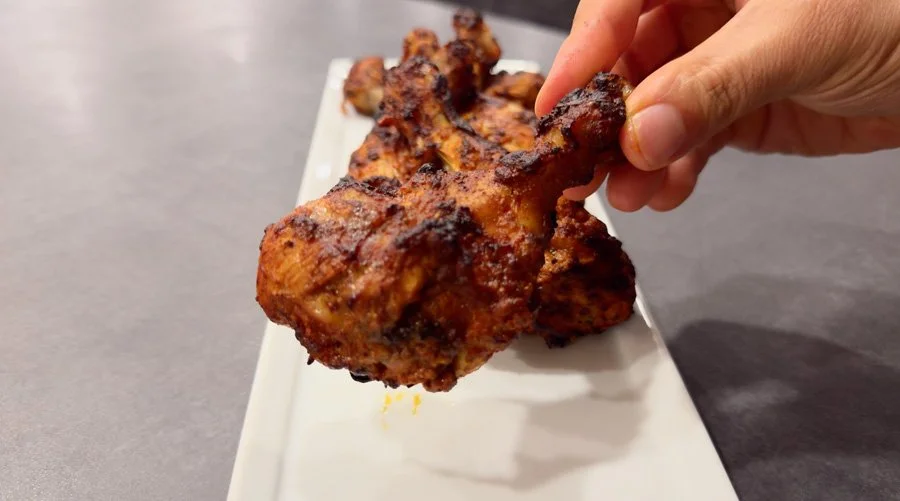 holding a piece of air fryer tandoori chicken